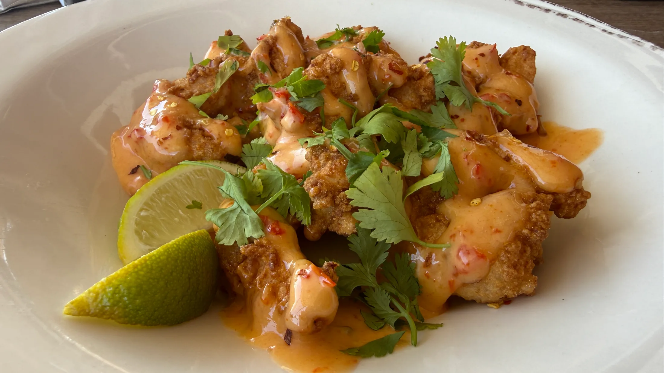 Denny Bar Company firecracker shrimp — crispy fried shrimp tossed in spicy orange sauce with chili flakes and fresh cilantro, served with lime