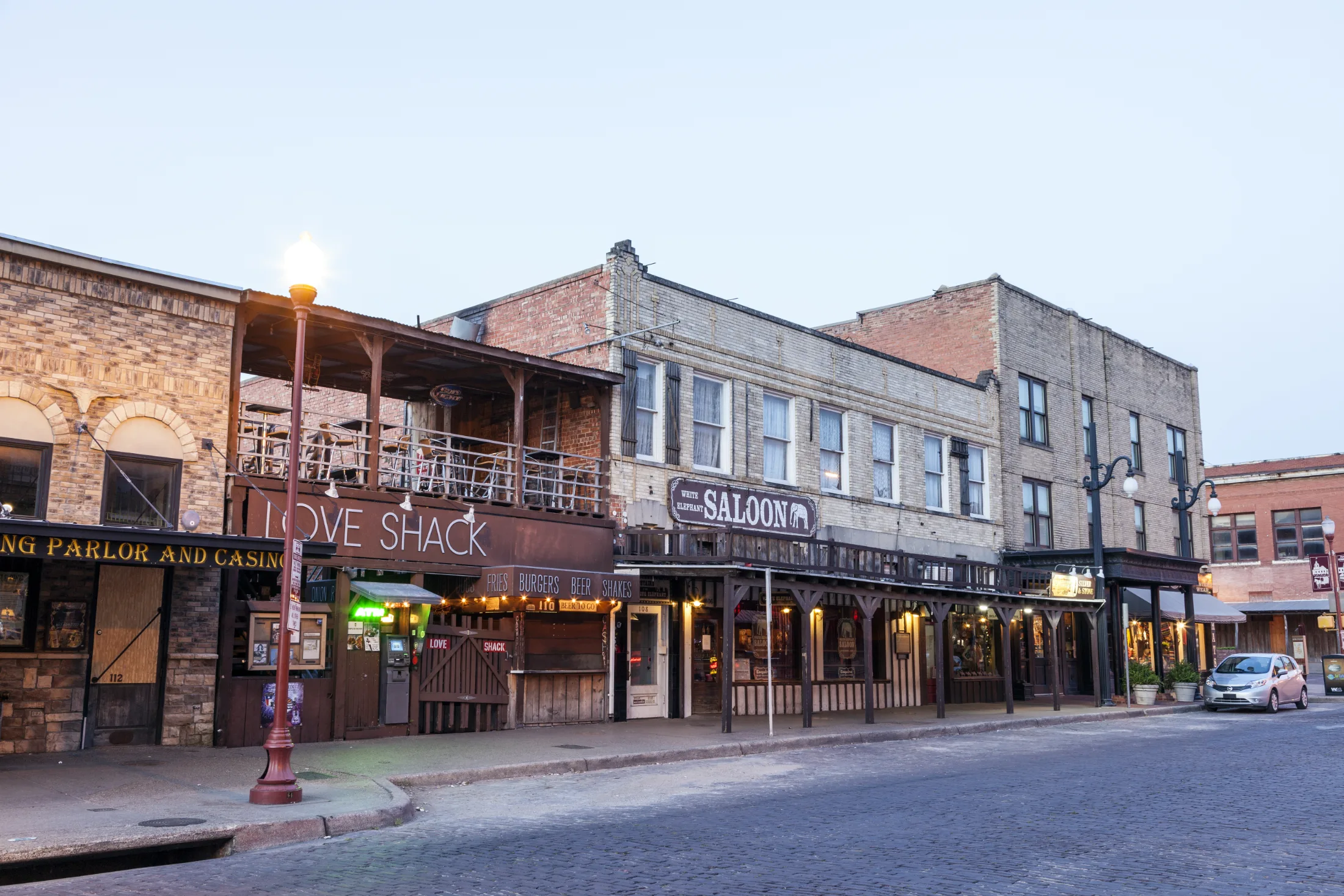 Dusk view of the historic Stockyards block showing Love Shack and White Elephant Saloon beneath old brick facades with warm window light