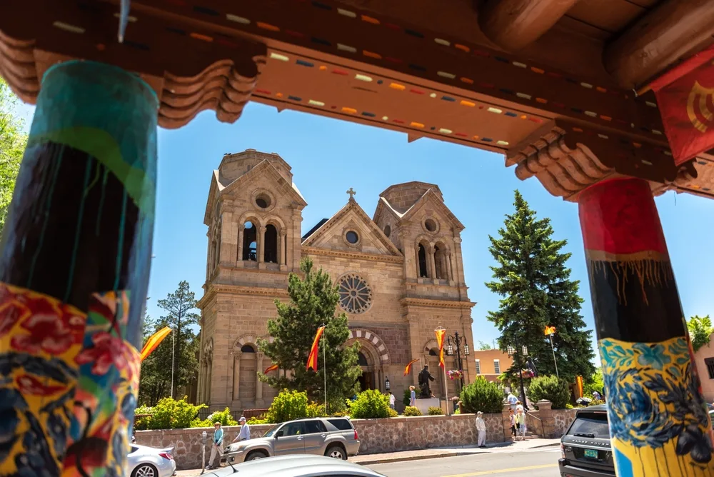 People strolling near the Cathedral Basilica of St. Francis, colorful flags in the breeze, bright midday sun