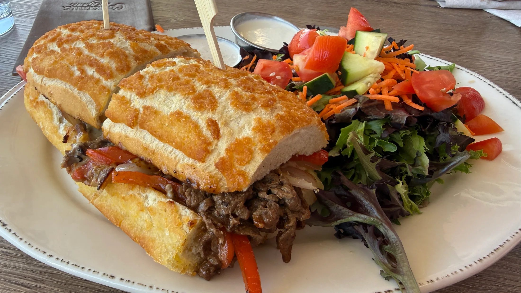 Denny Bar Company Philly cheesesteak sandwich with roasted red peppers and caramelized onions on a toasted roll, served with a mixed green salad