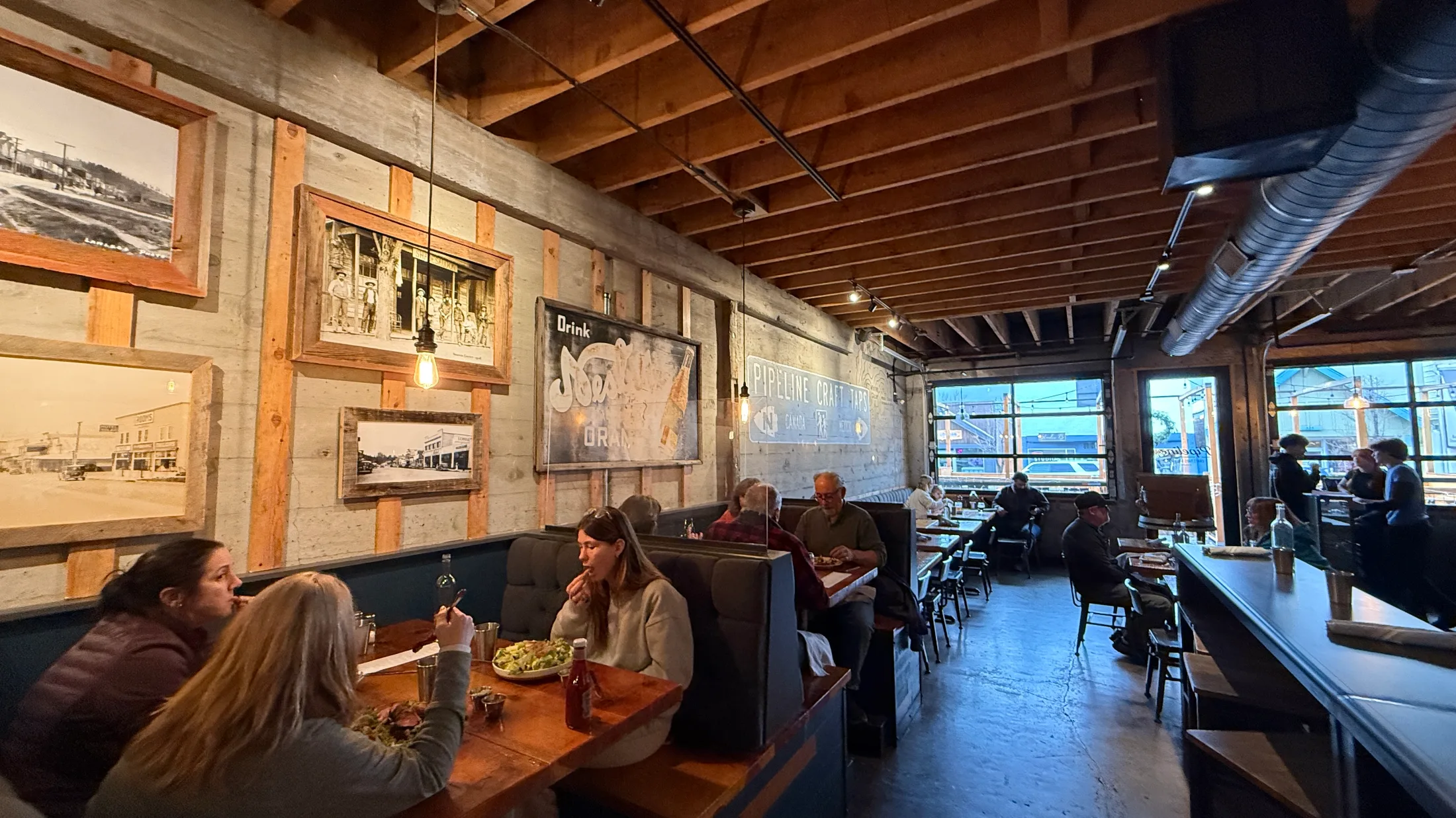 Interior dining room of Pipeline Craft Taps with booths, historical photos on the walls, and the garage door open to the boulevard