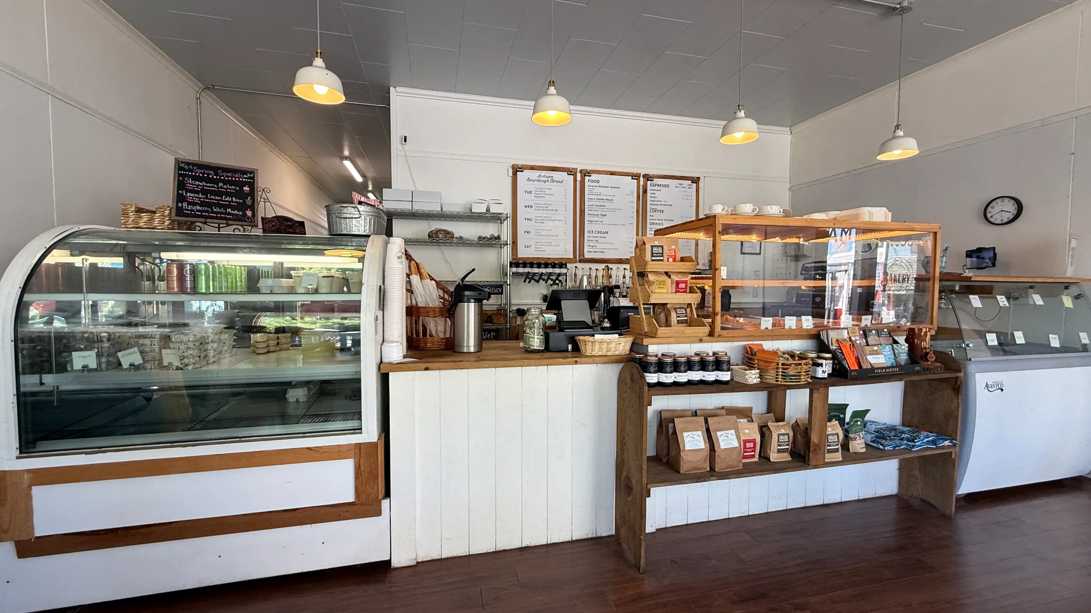 Full counter view of Farmhouse Bakery showing the pastry case, order counter, wood display shelving, and menu boards