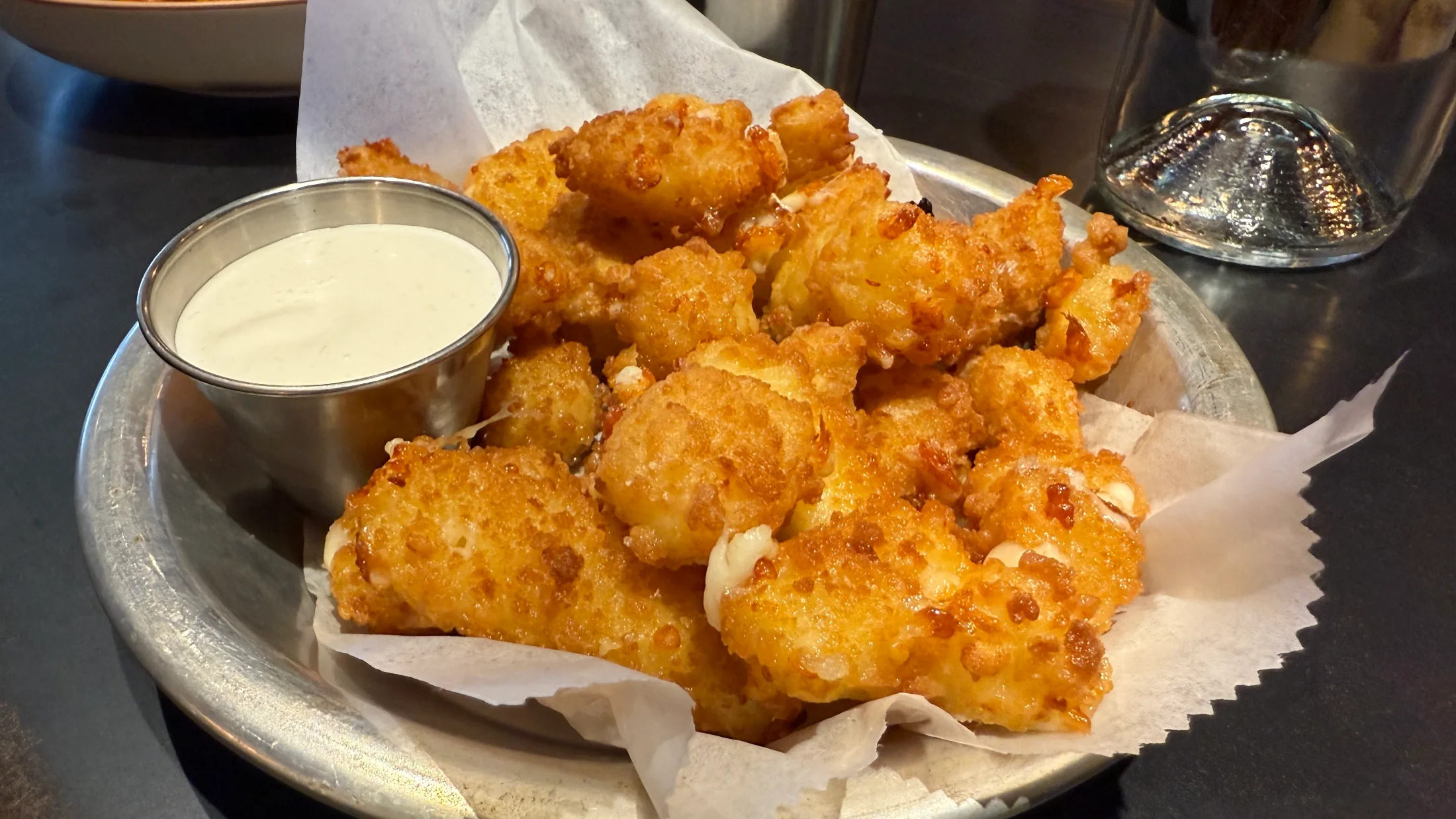 Fried cheese curds with a creamy dipping sauce in a metal basket at Pipeline Craft Taps