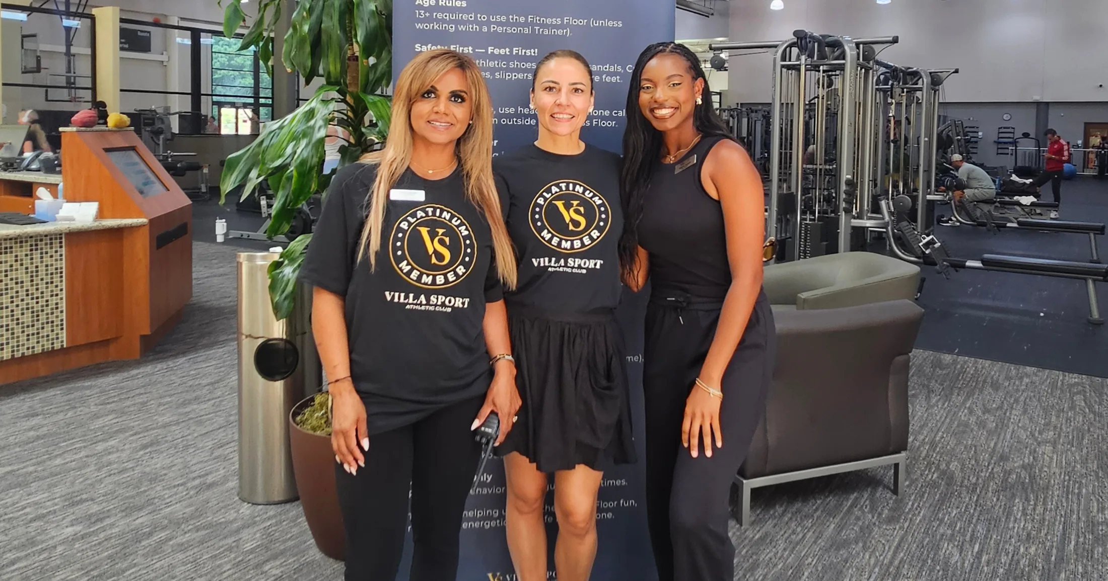 Three Villa Sport Platinum Member staff smiling together in front of the club's welcome banner