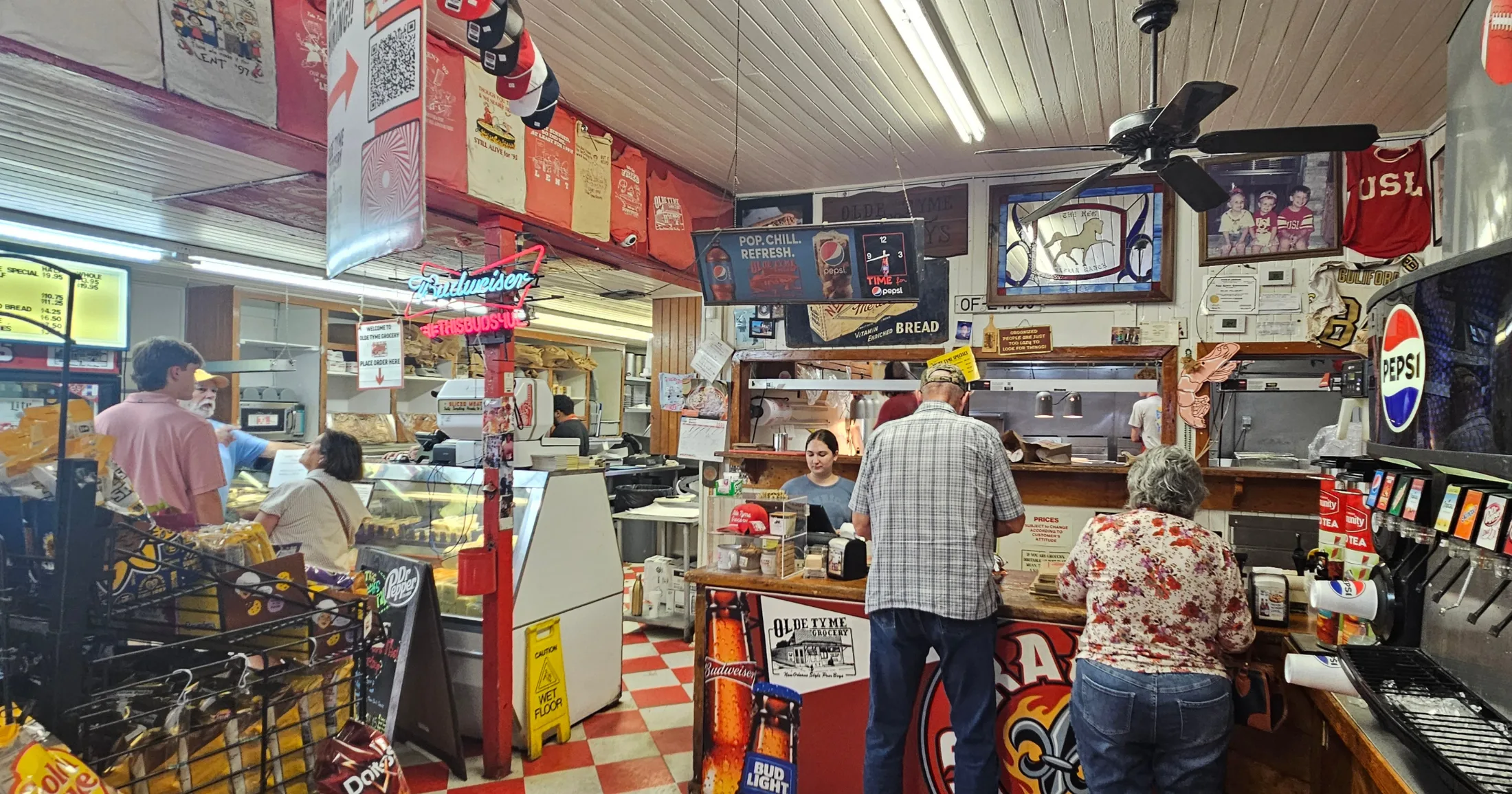 Inside Olde Tyme Grocery β red and white checkered floors, neon Budweiser sign, customers ordering at the counter