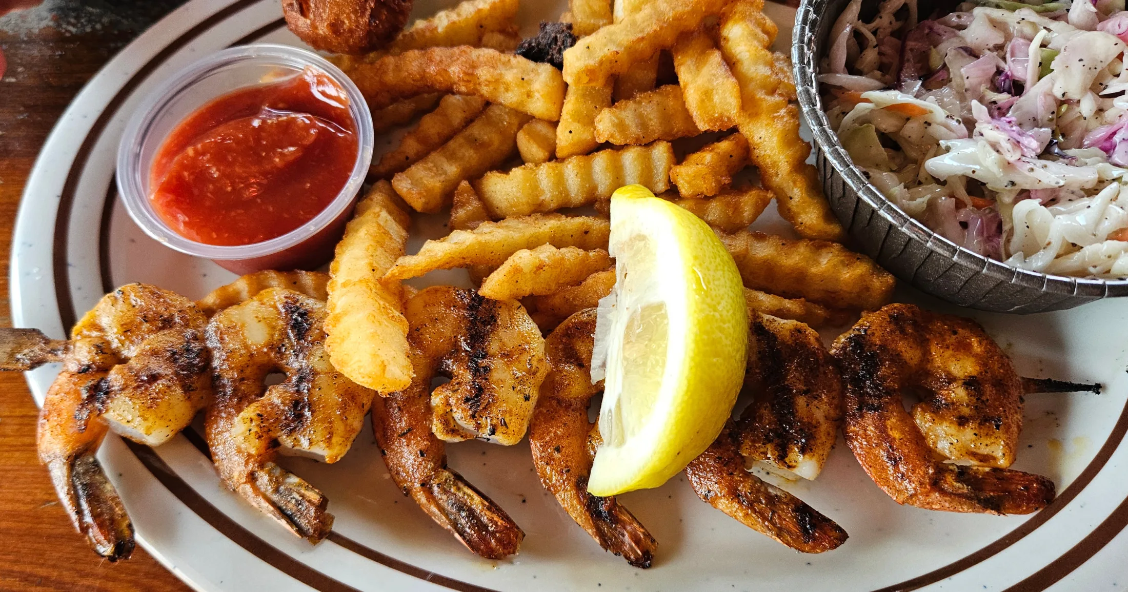 Grilled Shrimp skewer with crinkle fries served in a newspaper-lined basket