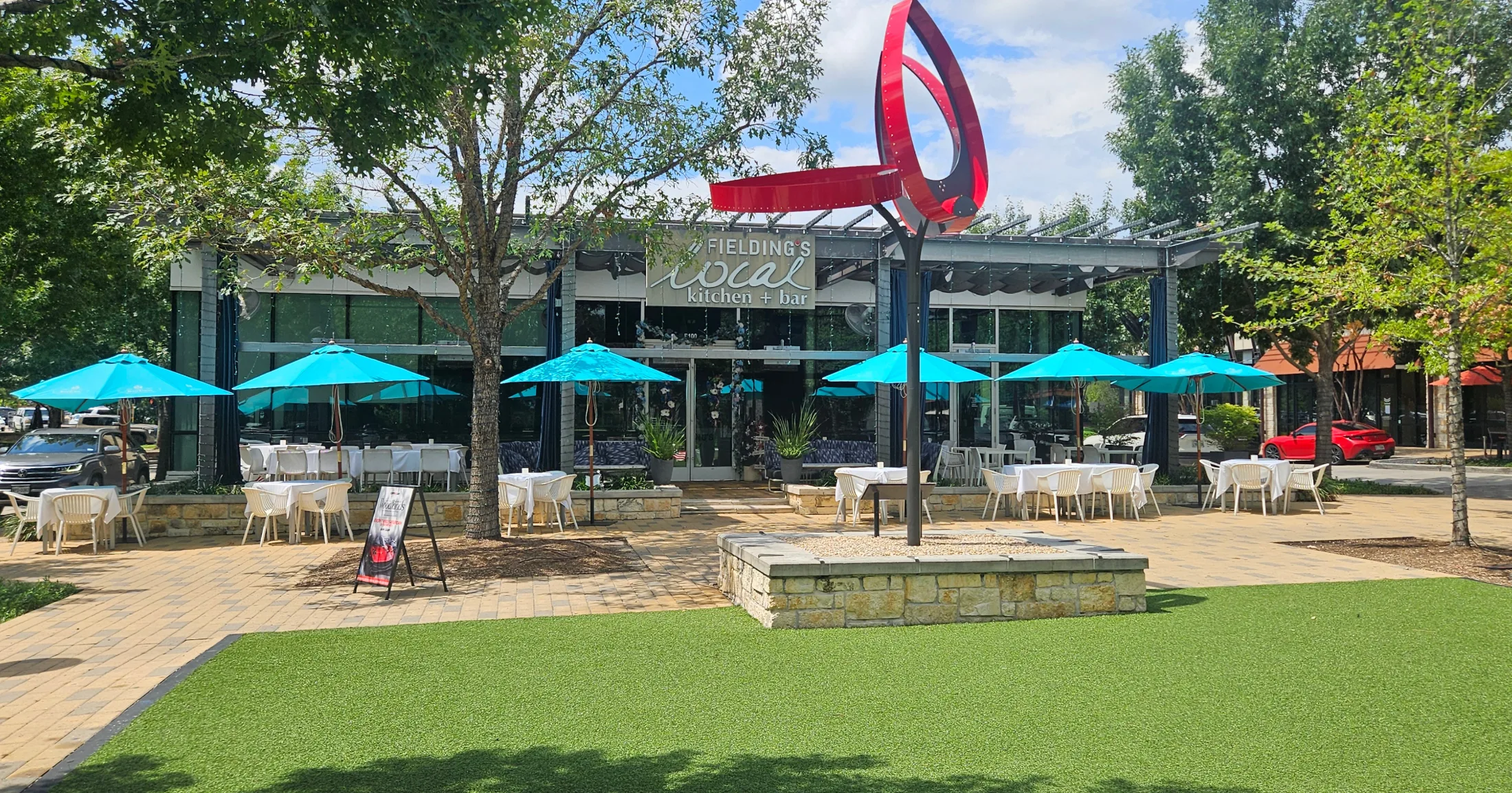 Fielding's Local Kitchen and Bar exterior with turquoise patio umbrellas and red sculpture at Creekside Village