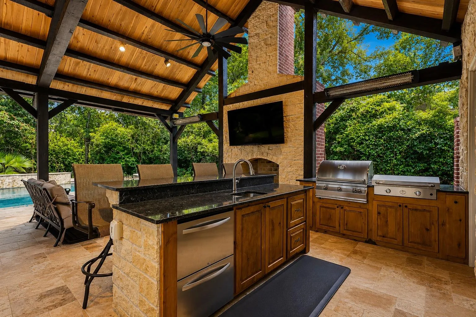 Covered outdoor kitchen with cedar ceiling, twin grills, granite counters, stone fireplace, and mounted TV at 7 Pastoral Pond Circle