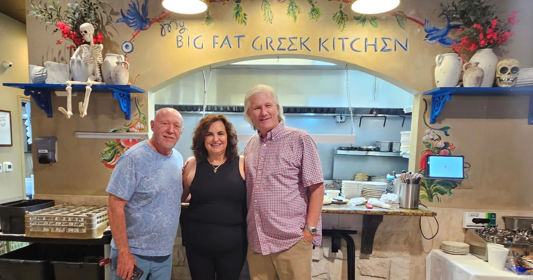 George Lindahl and the Mayor standing with Toula Huliaris in front of the My Big Fat Greek Kitchen mural at The Olive Oil