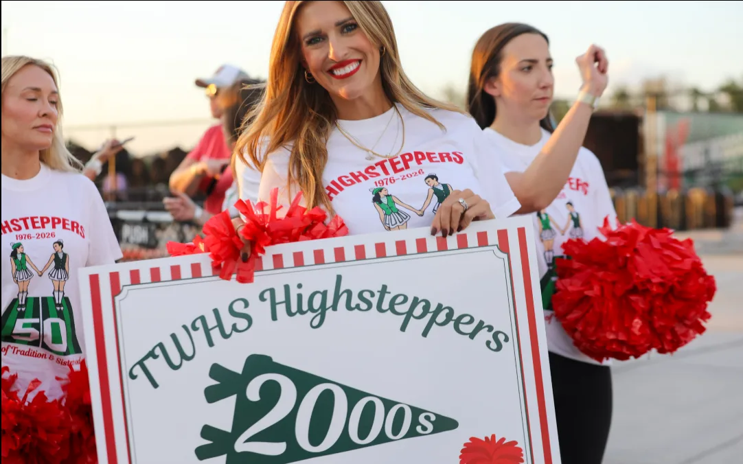 A smiling woman holds a TWHS Highsteppers 2000s sign surrounded by alumni in 50th anniversary shirts and red pom-poms