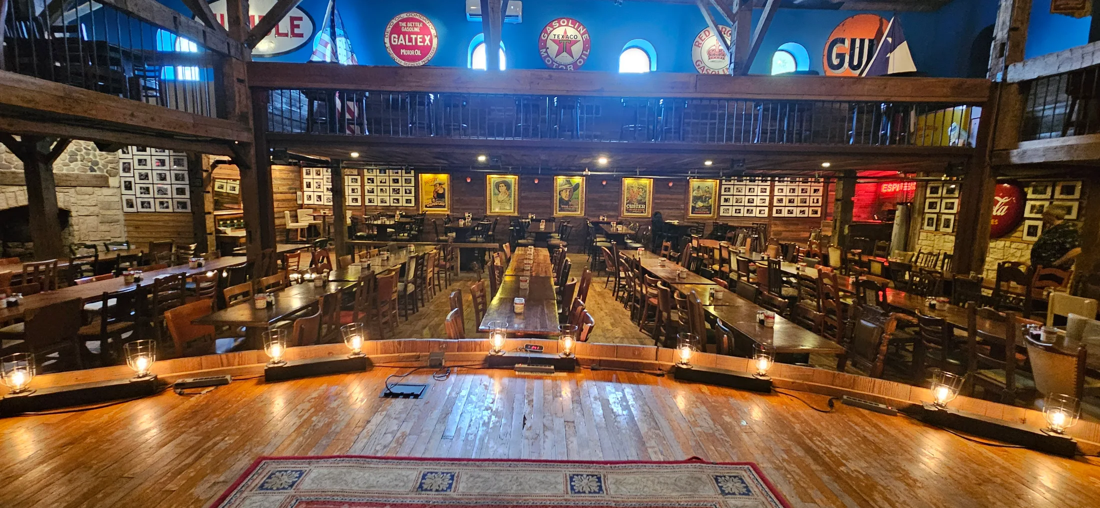 Stage-level view of Dosey Doe's main room, with lantern footlights, vintage Americana signage, and old-growth timber beams overhead