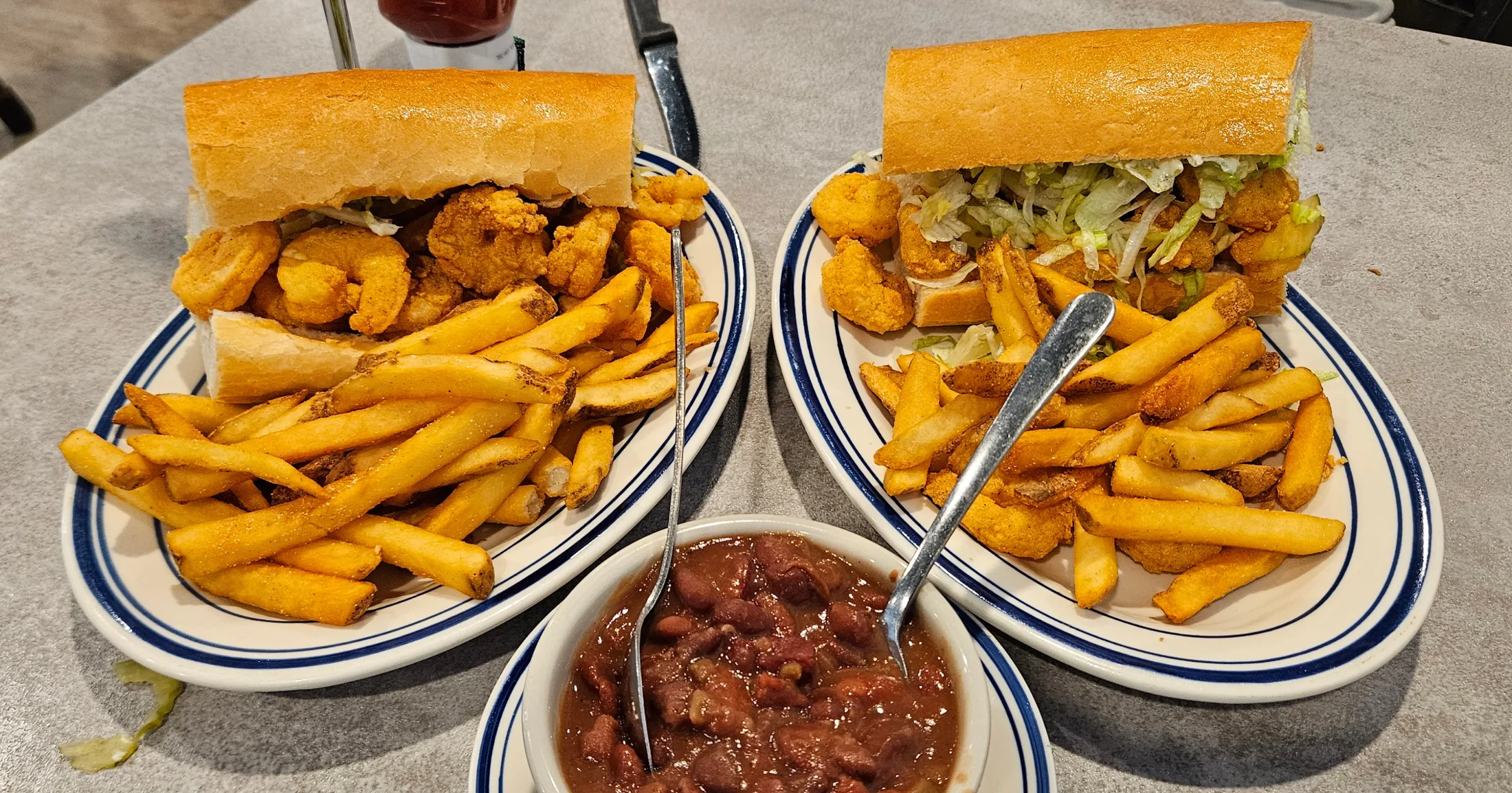 Two fried shrimp po-boys dressed with shredded lettuce, served with French fries and a bowl of red beans and rice