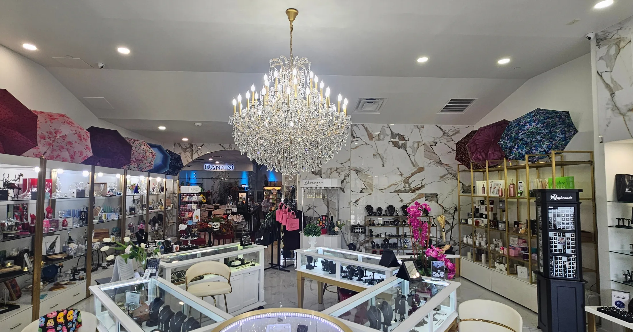 Dannini showroom floor with crystal chandelier overhead, jewelry display cases, colorful umbrellas, orchids, and gift merchandise filling the space