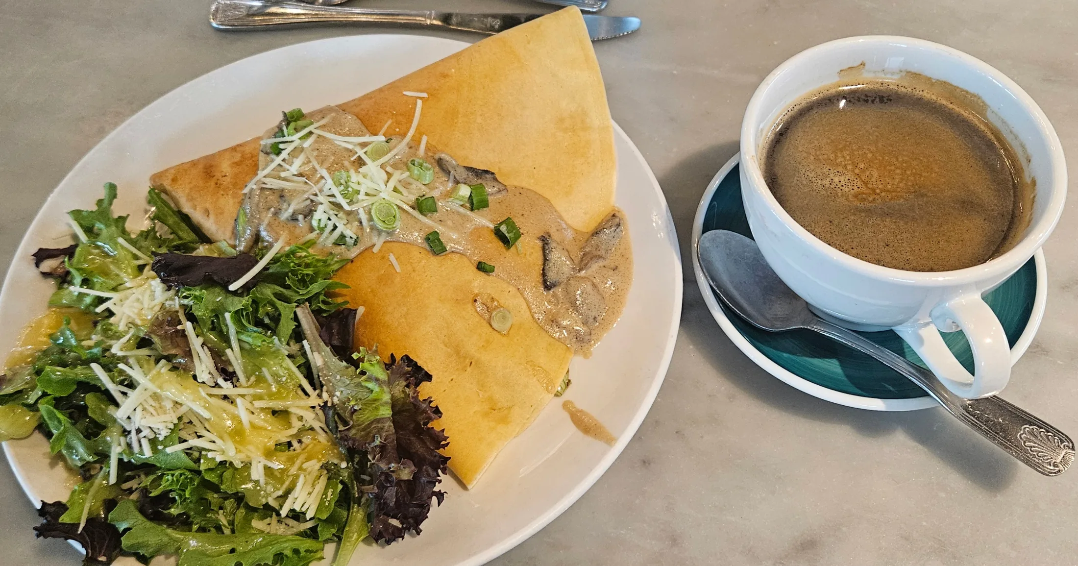 Savory crêpe with mushroom sauce, shaved cheese, scallions, and a side green salad, served with a café coffee