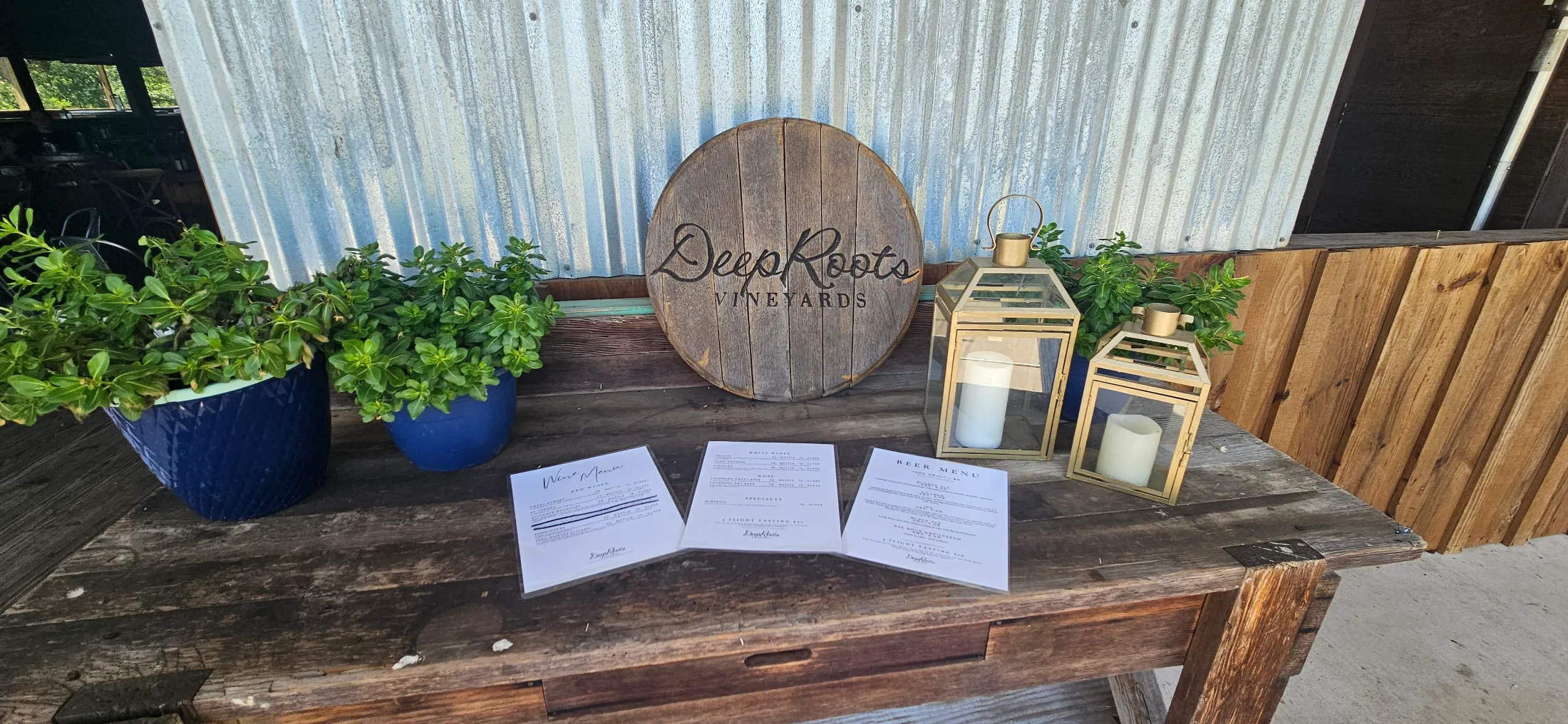 DeepRoots Vineyards welcome table with wine and beer menus, barrel-top sign, and gold lanterns