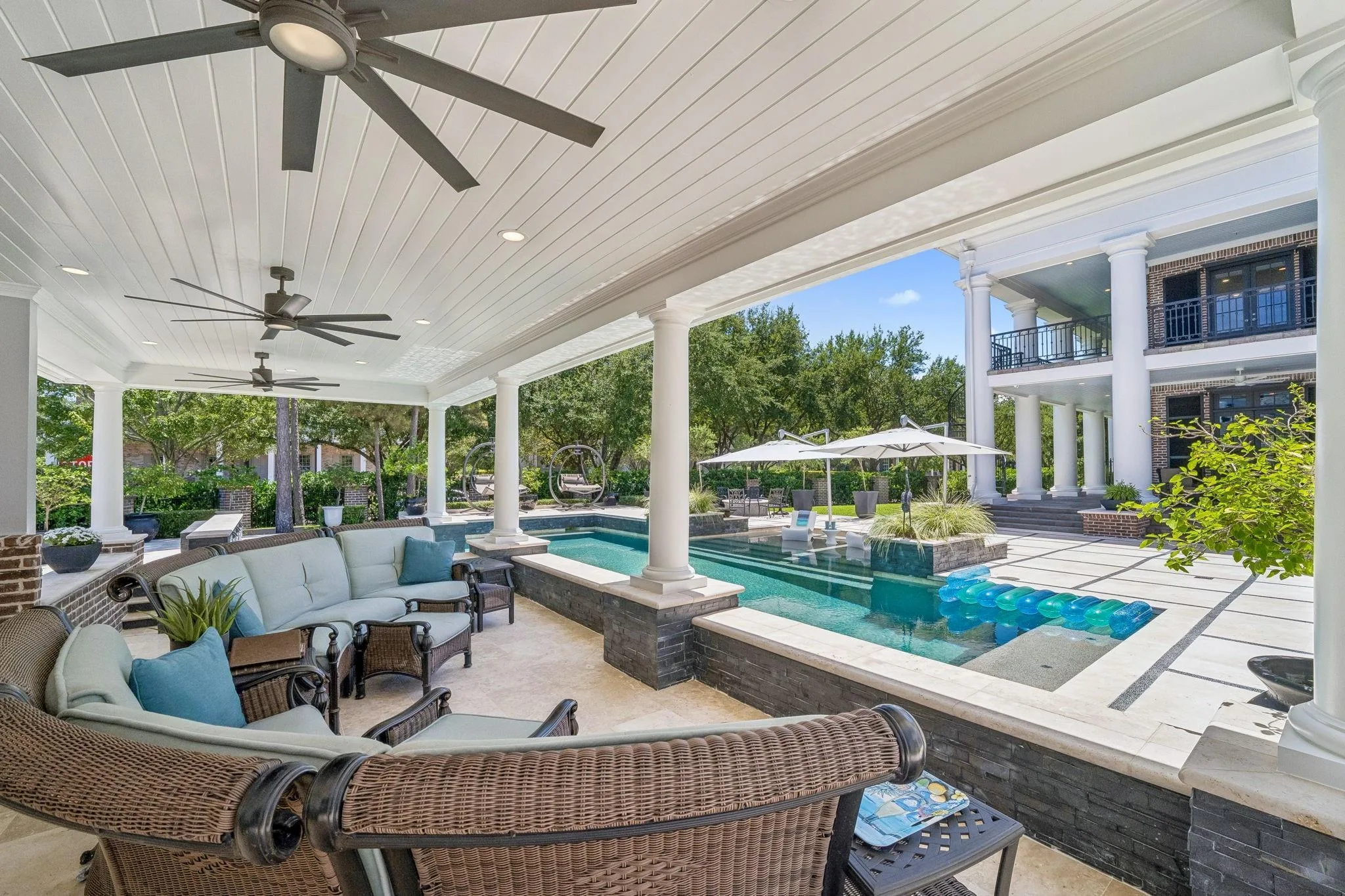 Covered outdoor living area at 2 Georgian Row with pool, spa, large ceiling fans, and white columns matching the home's Southern Colonial exterior