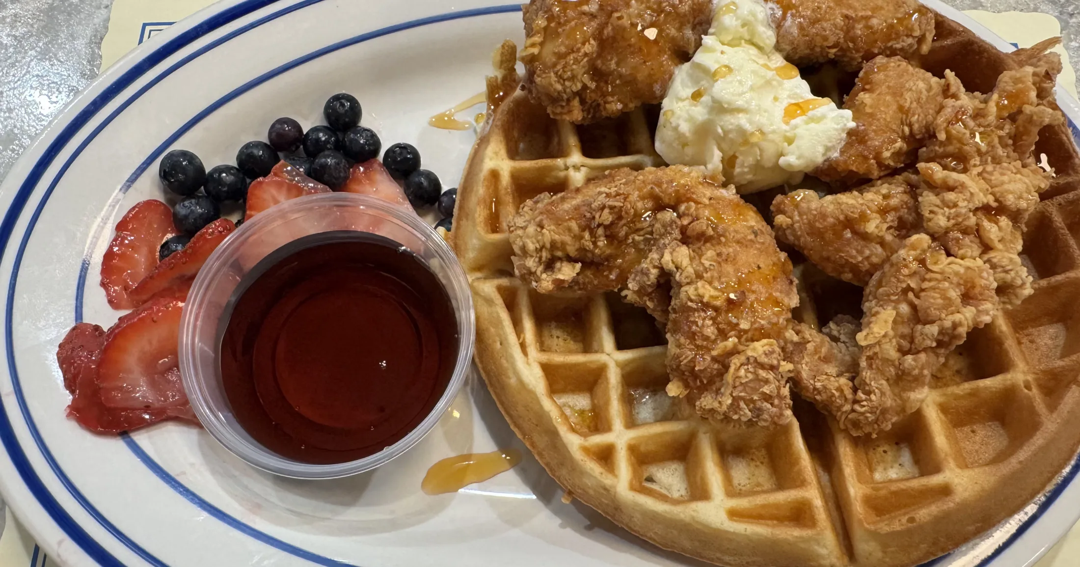 Chicken and waffles plate at The Downtowner with fried chicken tenders, golden waffle, whipped cream, honey drizzle, and fresh berries