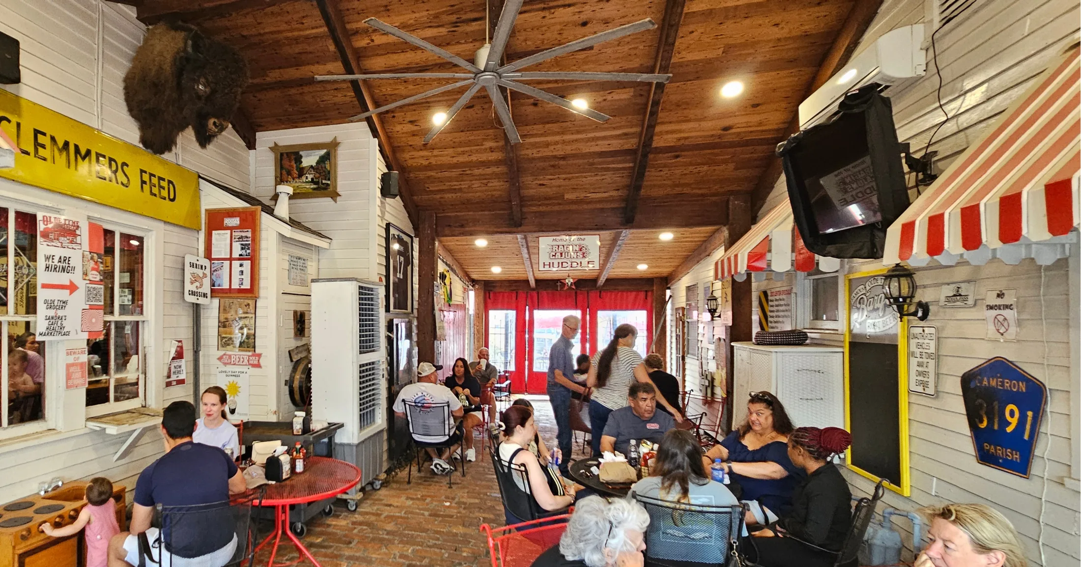 Dining area with exposed wood ceiling, large fan, brick floors, and the Raging Cajuns Huddle sign