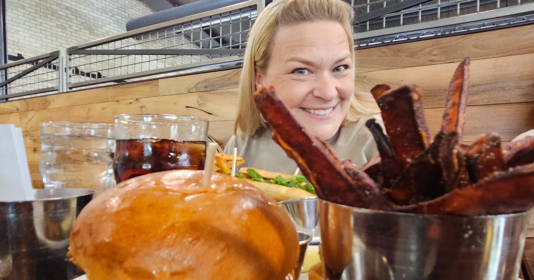 A founder smiling behind a table full of food including a brioche bun sandwich, ribs, and drinks at Farmers Brewing Co. in Chico