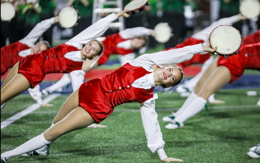 TWHS Highsteppers extend their arms holding tambourines in a floor-level performance pose under the stadium lights