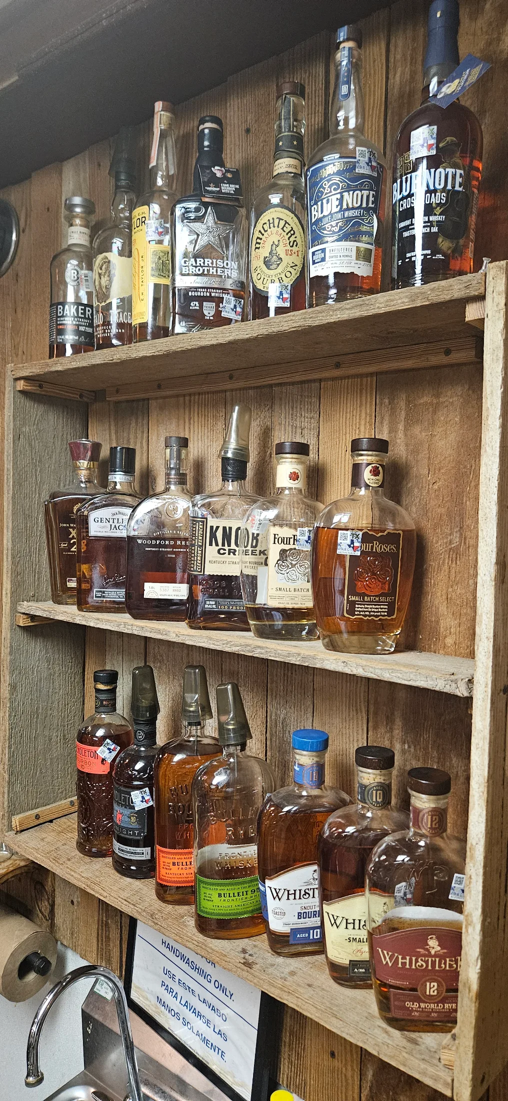 Rustic wooden bar shelves at Dosey Doe lined with bottles of Garrison Brothers, Woodford Reserve, Knob Creek, Four Roses, Whistler, and other bourbons and whiskeys