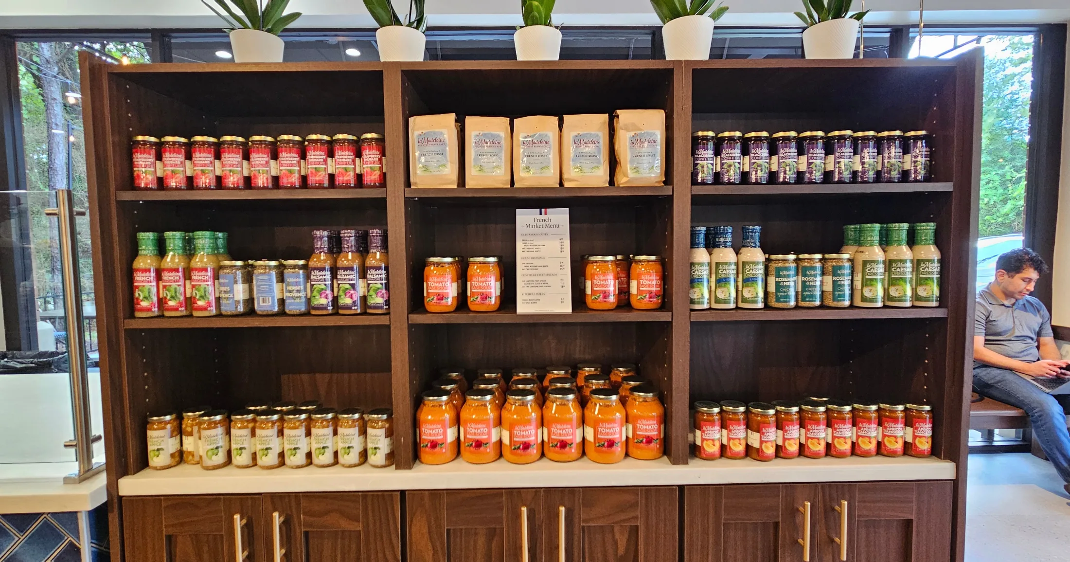 La Madeleine French Market retail shelf stocked with branded jarred sauces, dressings, jams, and coffee bags