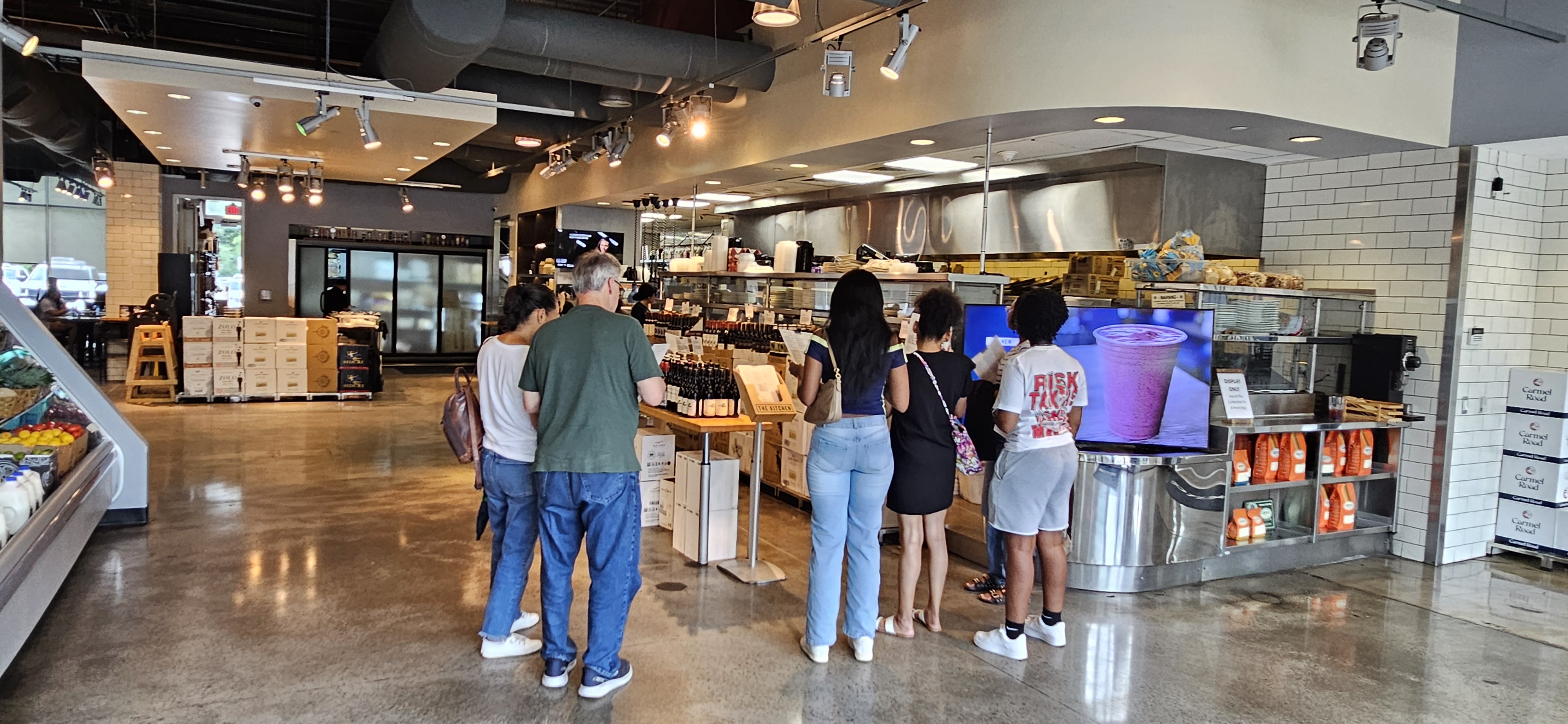 Customers ordering lunch at The Kitchen's open counter with the bustling open kitchen visible behind them
