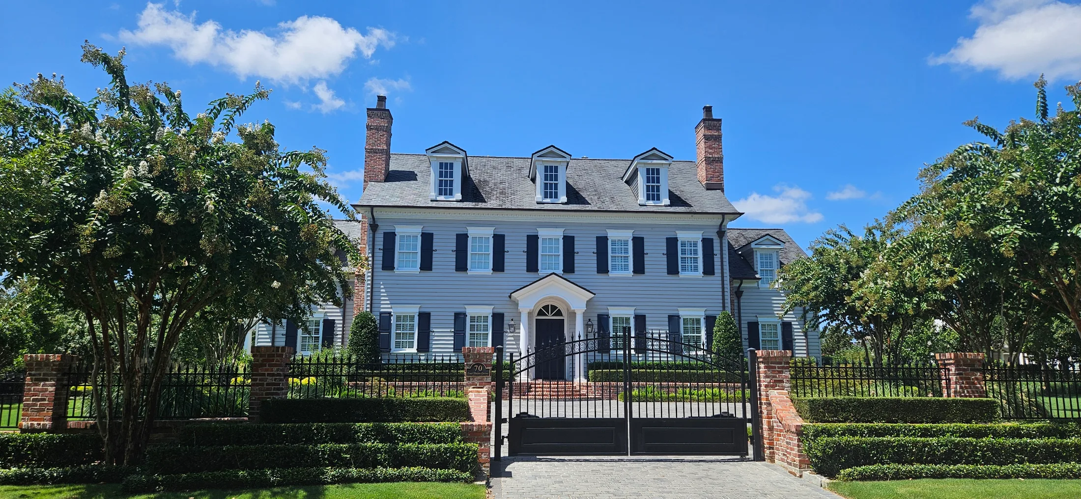 Colonial Revival home in East Shore with gray clapboard siding, black shutters, twin brick chimneys, three dormers, and gated brick entry
