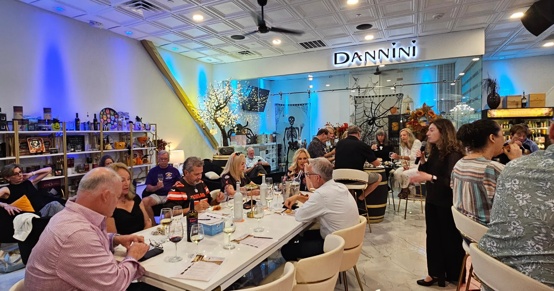 Dannini boutique event night with guests gathered at tables for a wine tasting, blue ambient lighting and Halloween decor in the background