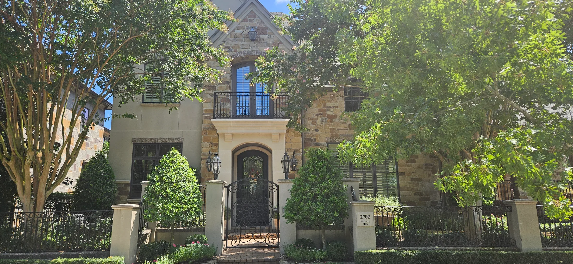 Stone and stucco home in East Shore, The Woodlands, with wrought iron entry gate, gas lanterns, and Juliet balcony