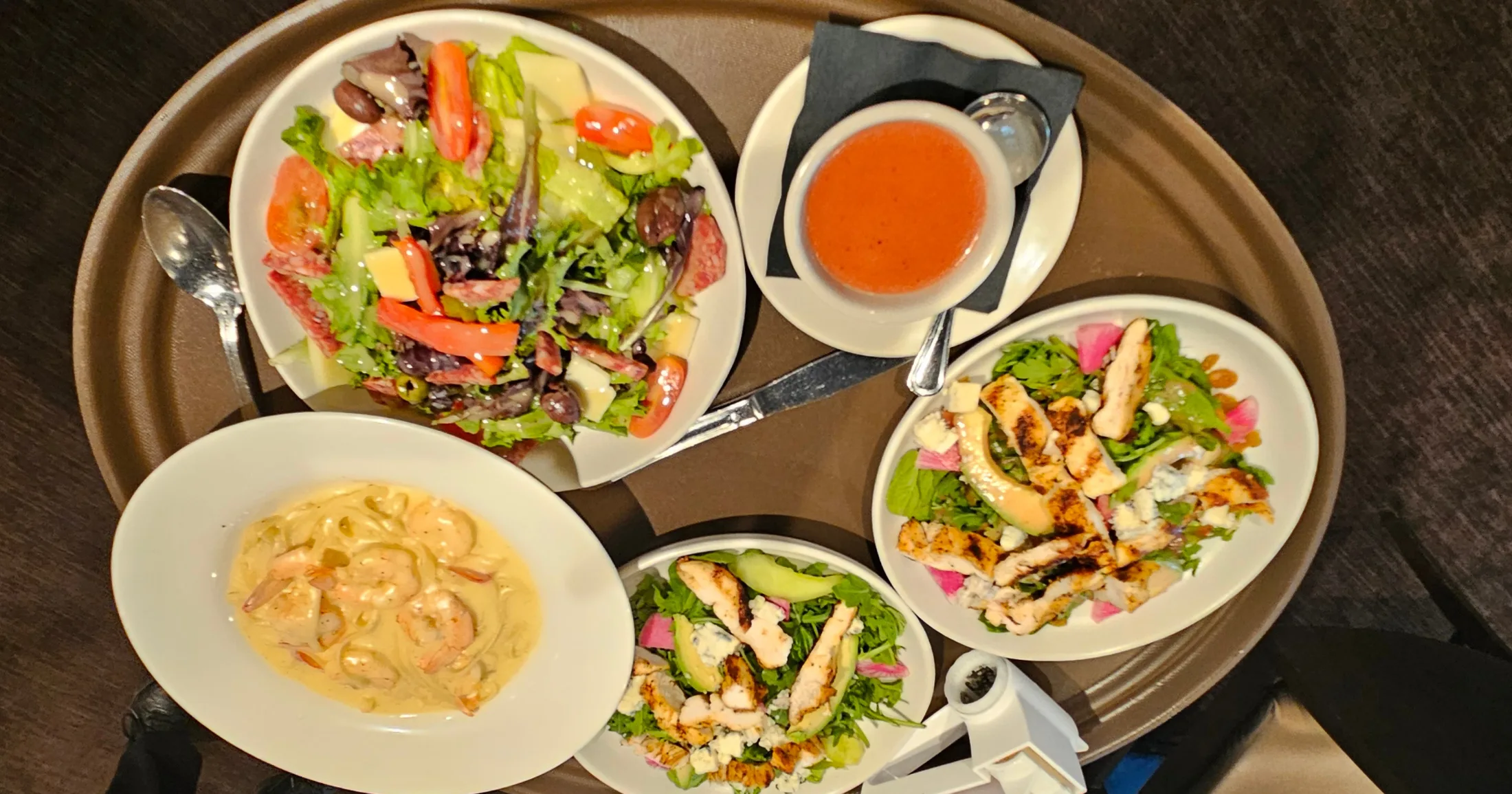 Overhead tray showing antipasto salad, tomato bisque, grilled chicken arugula salad, and shrimp pasta