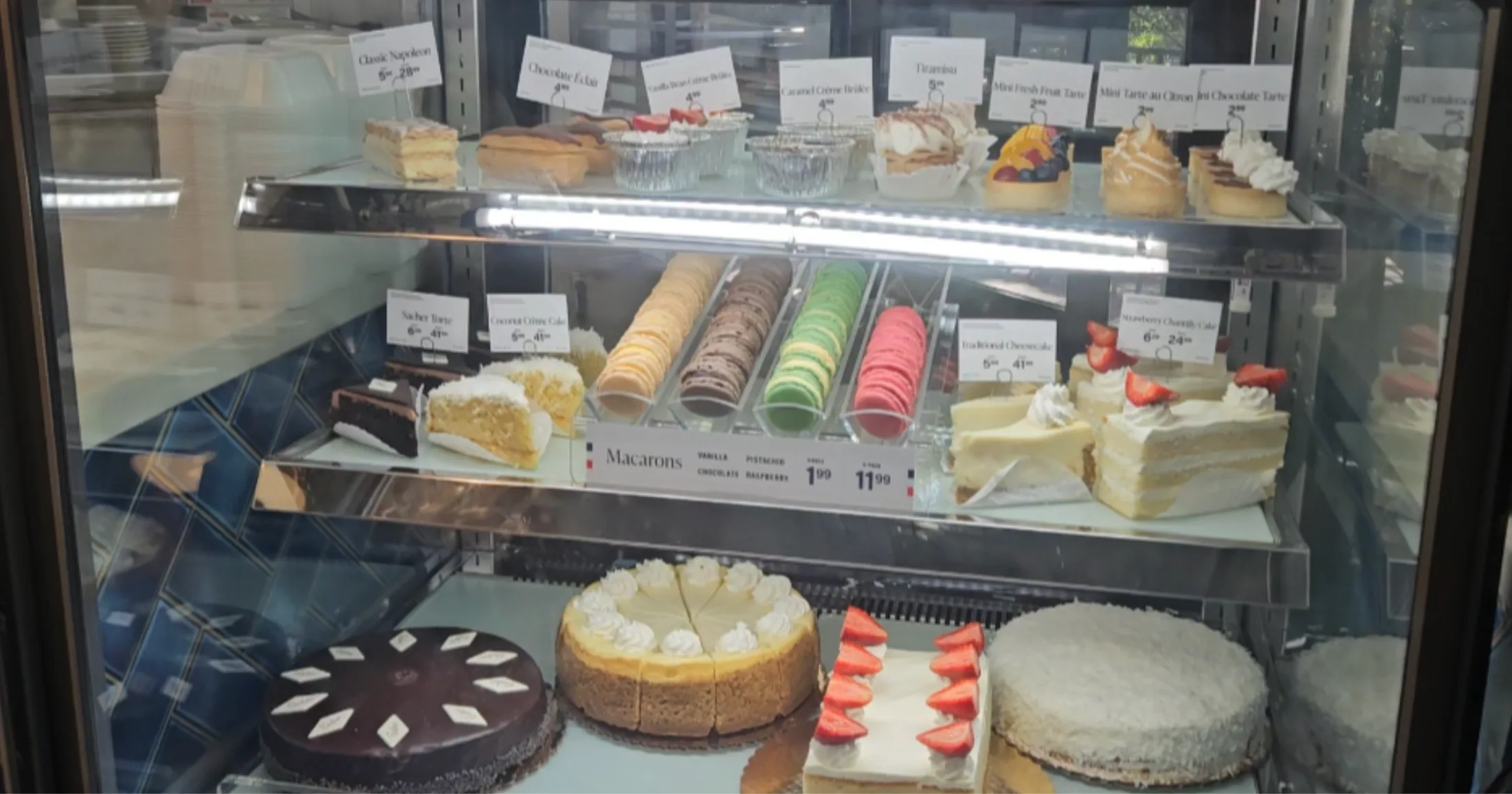 La Madeleine's pastry and dessert case displaying macarons, Napoleon slices, crème brûlée, cheesecake, and fruit tarts