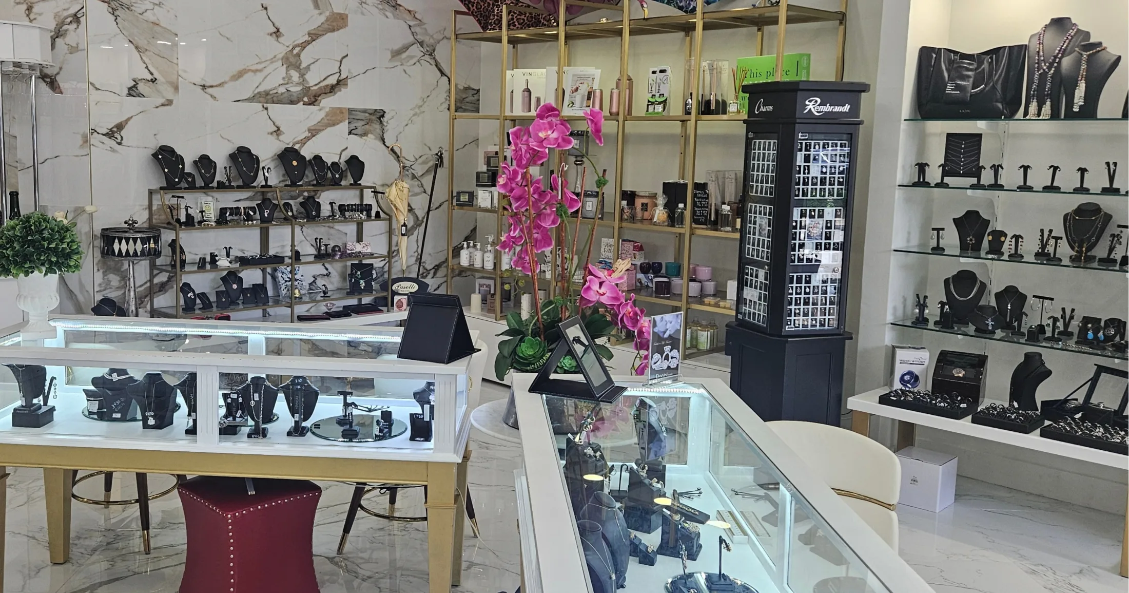 Dannini jewelry display cases with necklaces, rings, and earrings under bright lighting, pink orchids on the counter and Rembrandt charms tower nearby