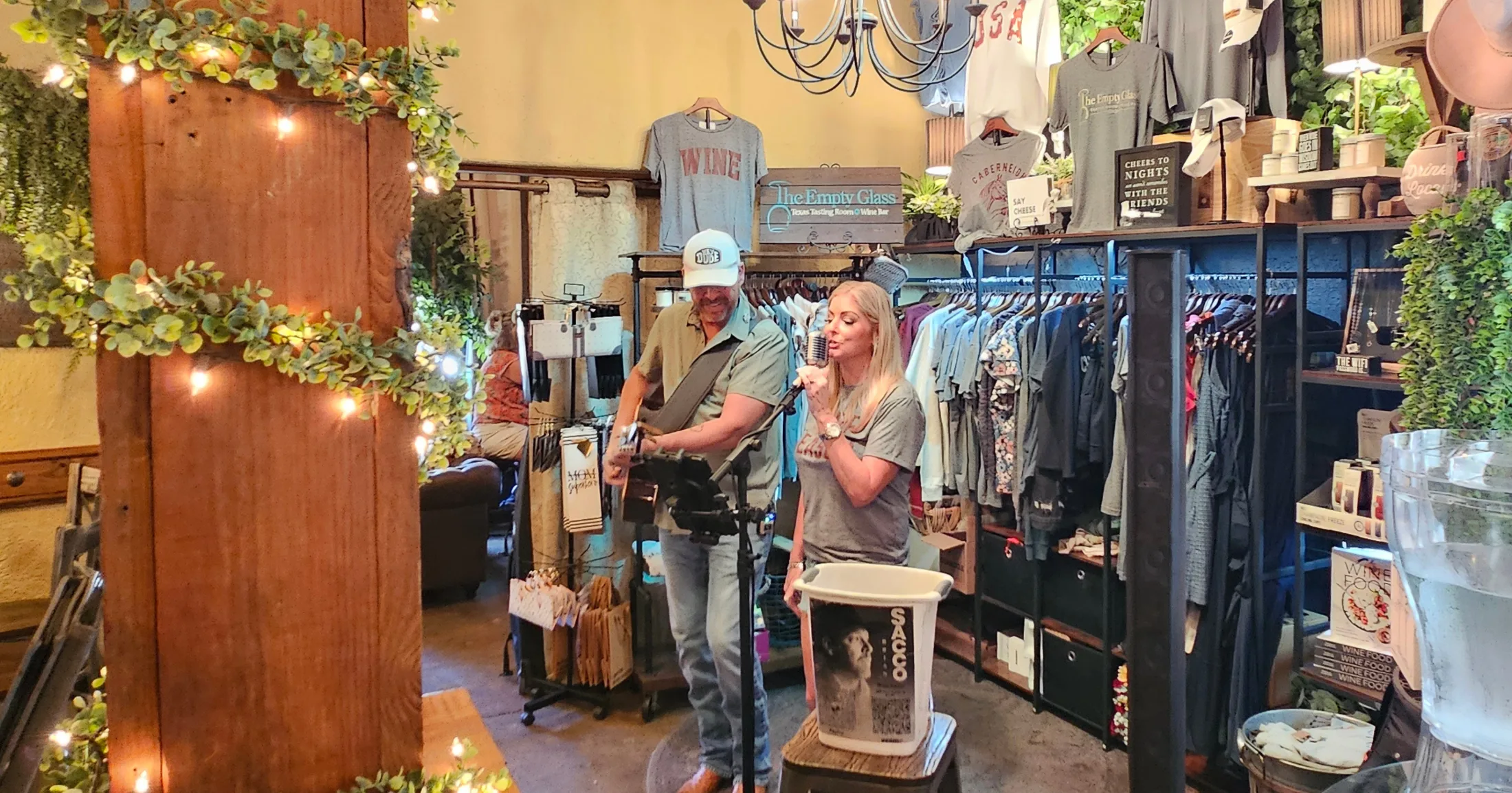 Brian and Dana Sacco performing live music inside The Empty Glass tasting room, surrounded by retail merchandise and string lights