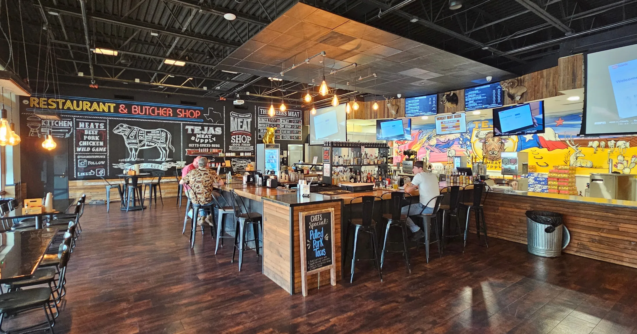 Tejas Meat Supply bar and restaurant interior showing chalkboard menu, bar seating, and large dining area