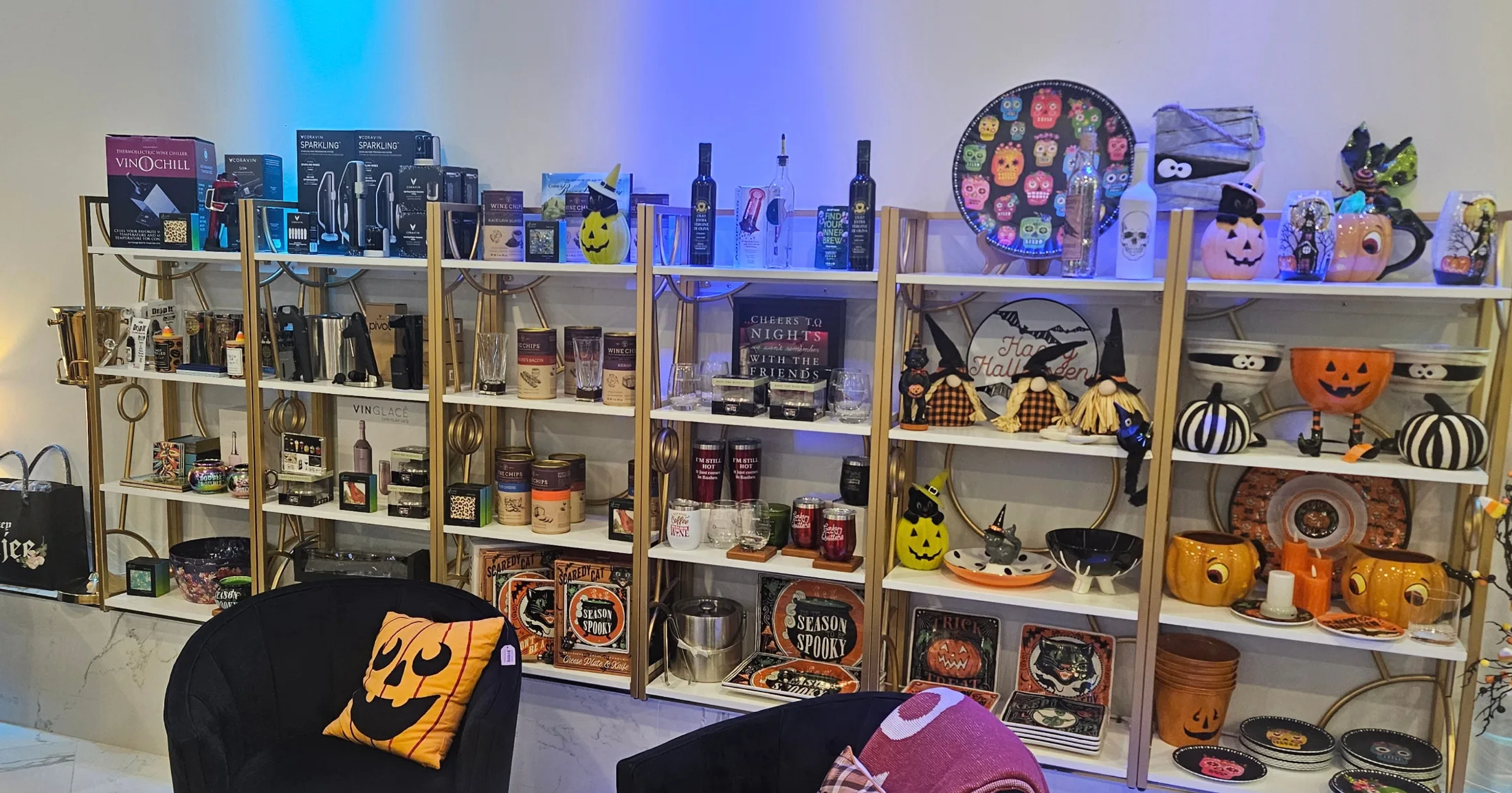 Dannini gift and decor wall with seasonal Halloween merchandise, wine accessories, barware, and holiday-themed items on white and gold shelving