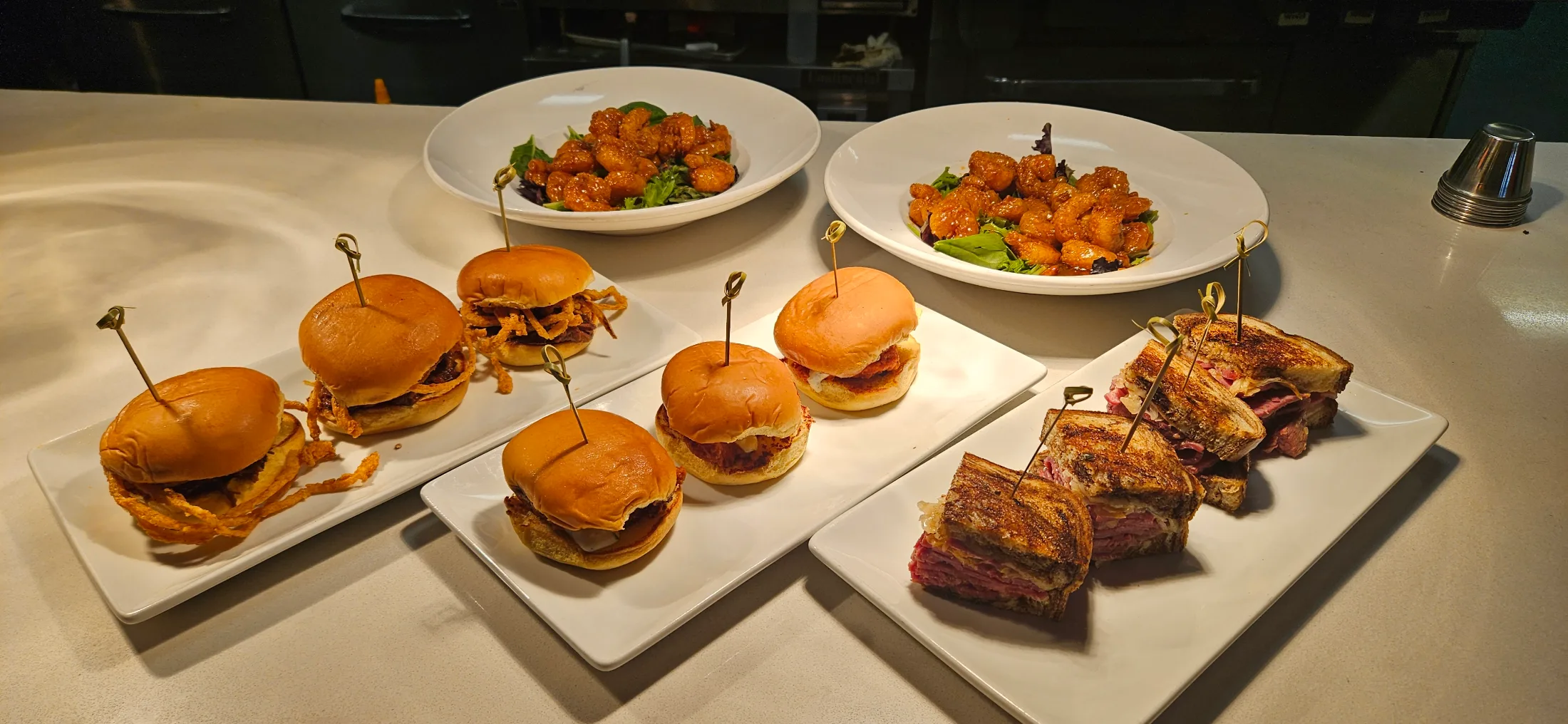 Spread of sliders, bam bam shrimp, and sandwiches on white plates at Federal American Grill