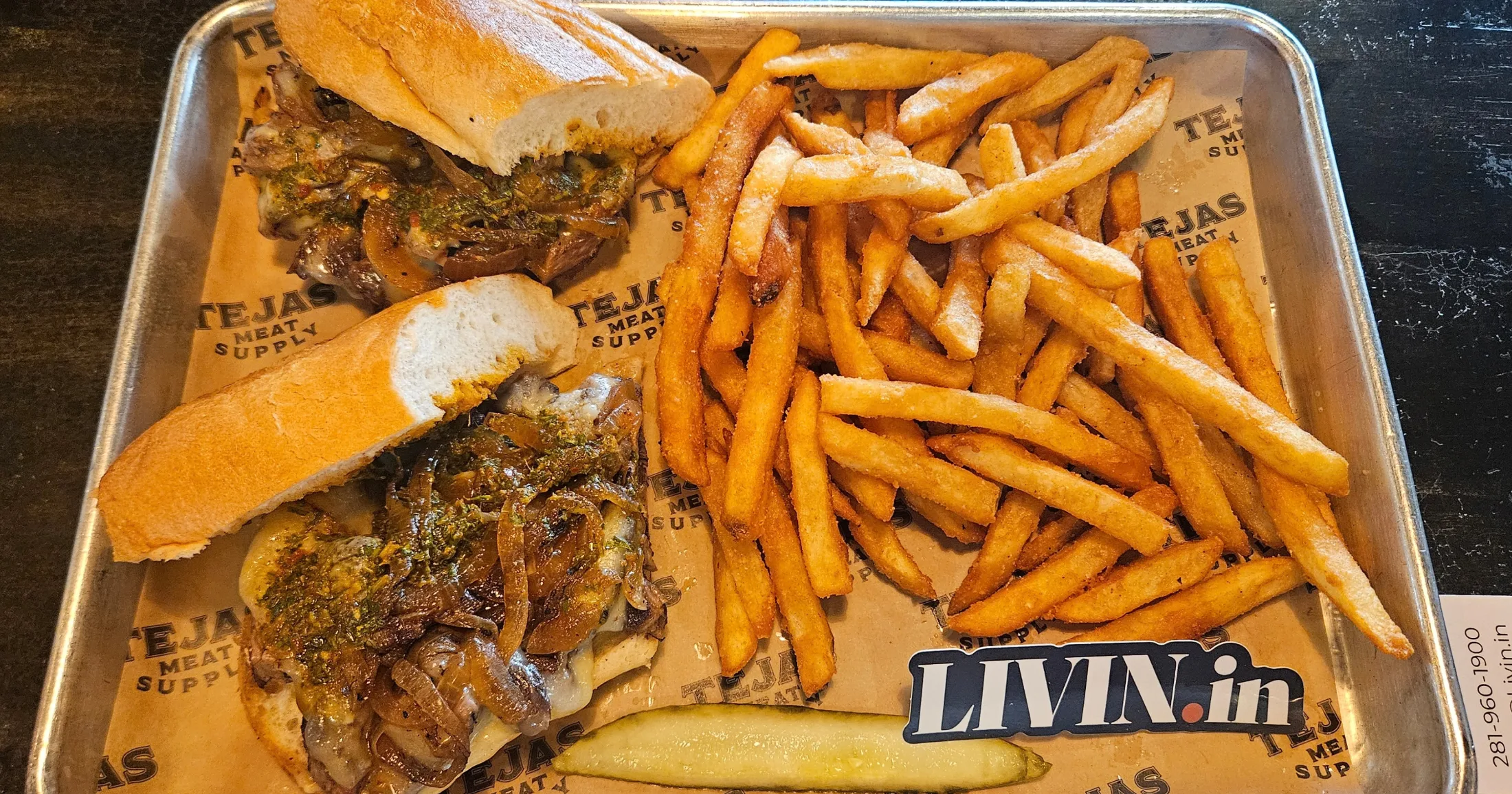 Tejas Meat Supply steak sandwich on a hoagie roll with caramelized onions, herb sauce, and fries on a metal tray