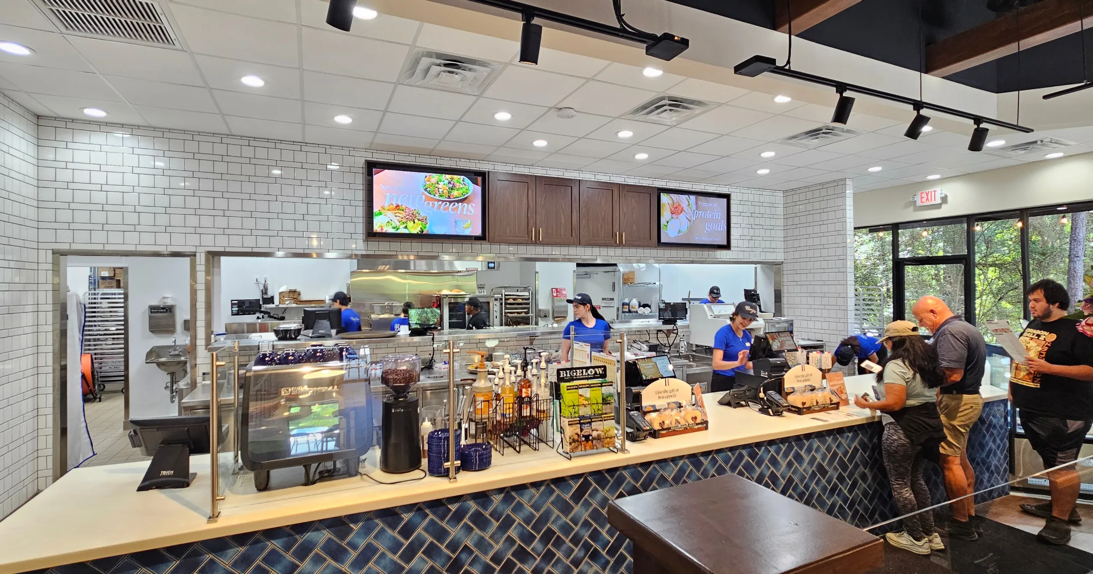 La Madeleine's open kitchen counter with staff working during a busy opening week, customers ordering at the register