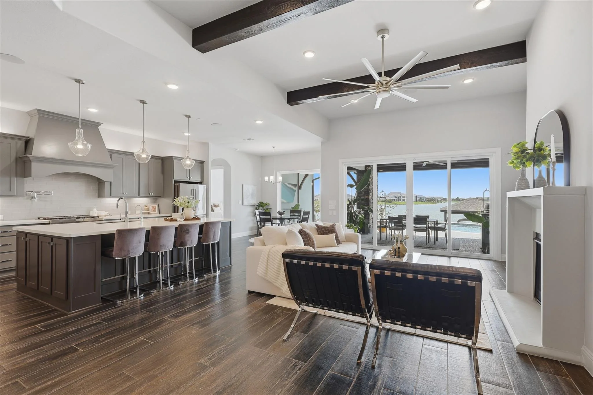 Open great room with dark wood beam ceilings, large kitchen island, and sliding glass doors opening to the pool and lake