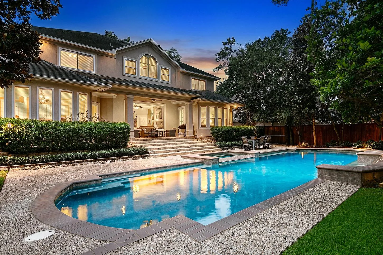 Resort-style backyard pool and spa with fountain features, covered lanai, and manicured lawn at dusk