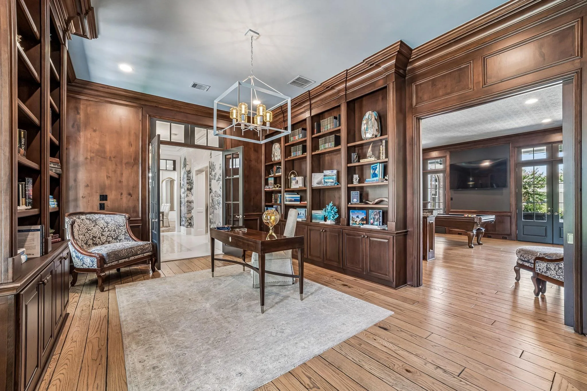 Wood-paneled library and study at 2 Georgian Row with floor-to-ceiling built-in bookshelves and a modern chandelier