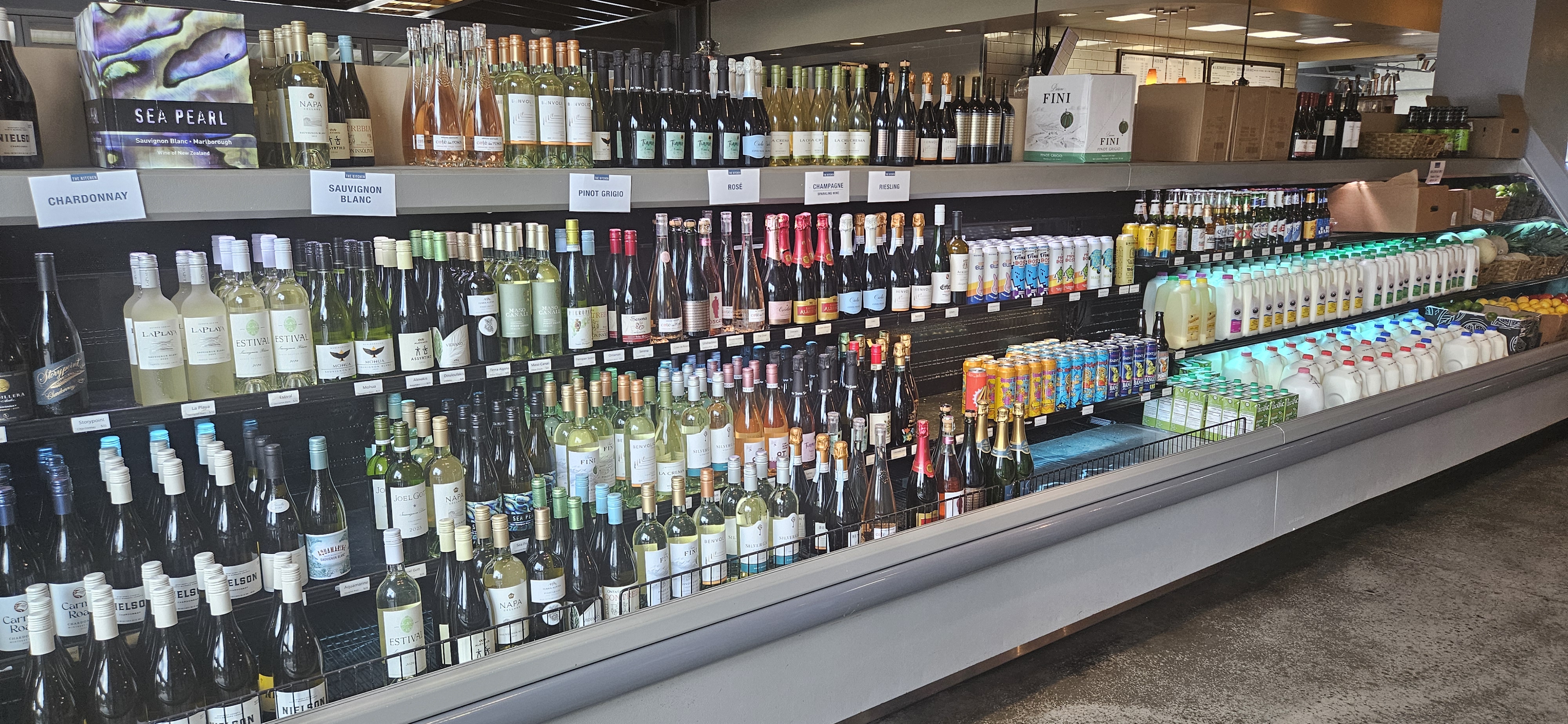 Wall-length refrigerated wine market at The Kitchen organized by varietal β Chardonnay, Sauvignon Blanc, Pinot Grigio, RosΓ©, Champagne, and Riesling