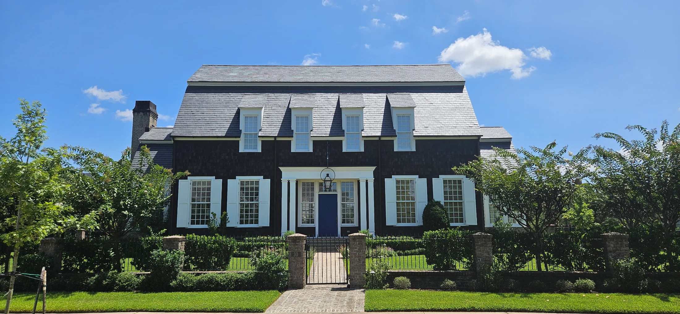 Second Empire style home in East Shore with dark shingle siding, wide mansard slate roof, white shutters, and navy blue front door