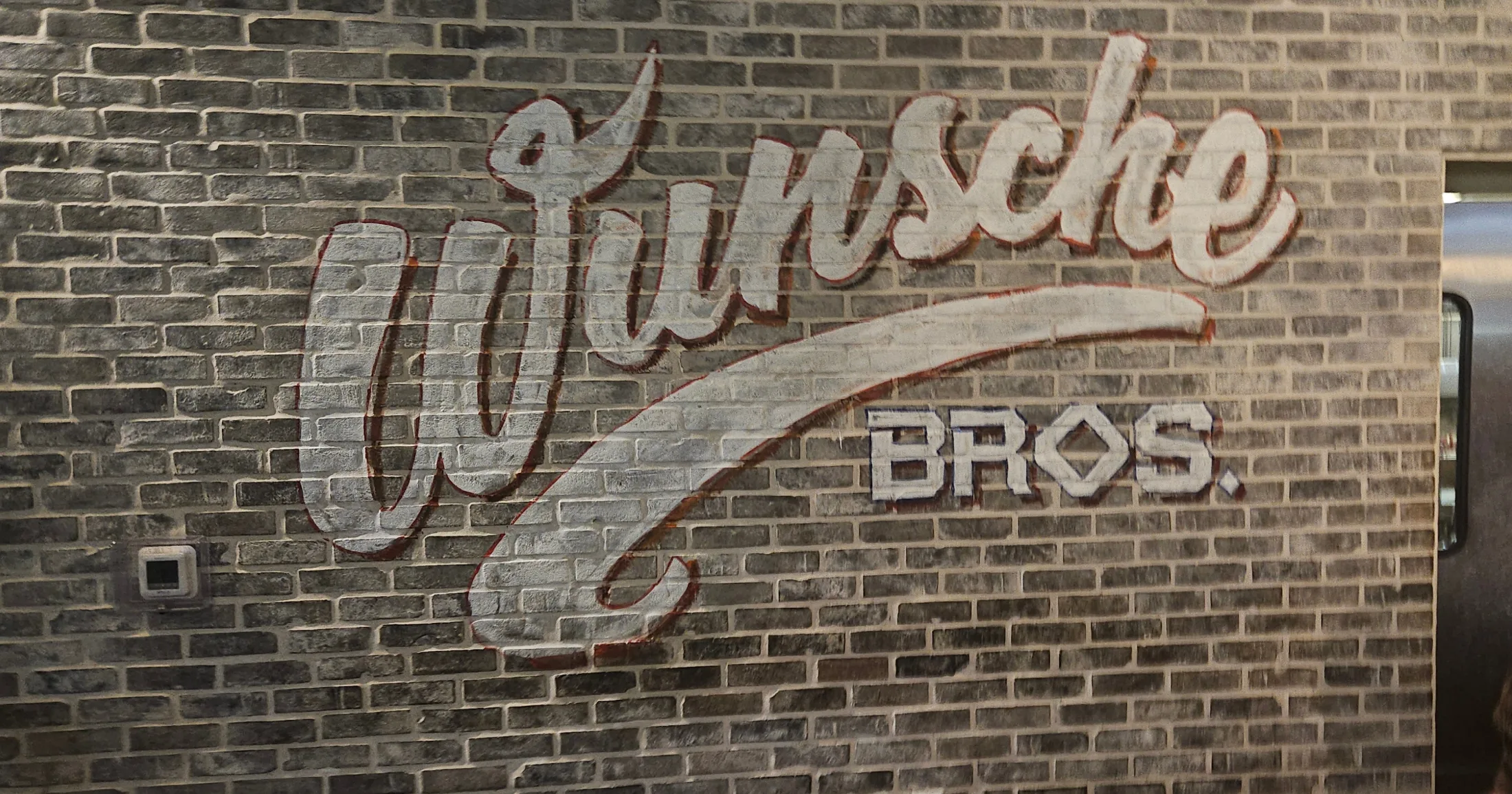 Wunsche Bros. logo painted on a grey brick wall