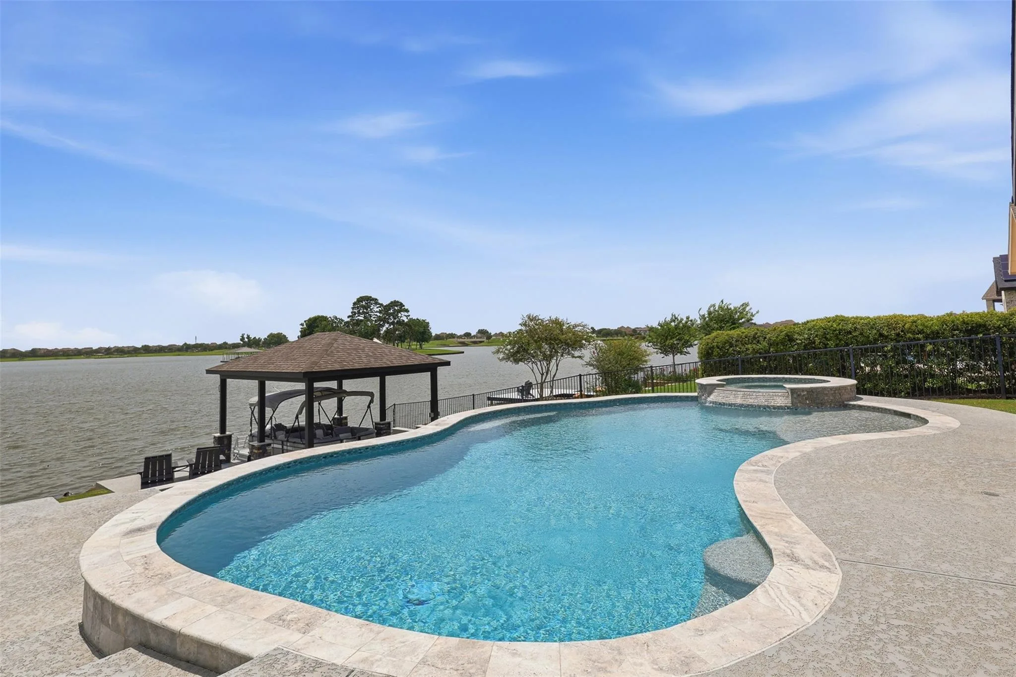 Freeform pool and spa with travertine decking, covered boat dock, and wide open lake view behind the property