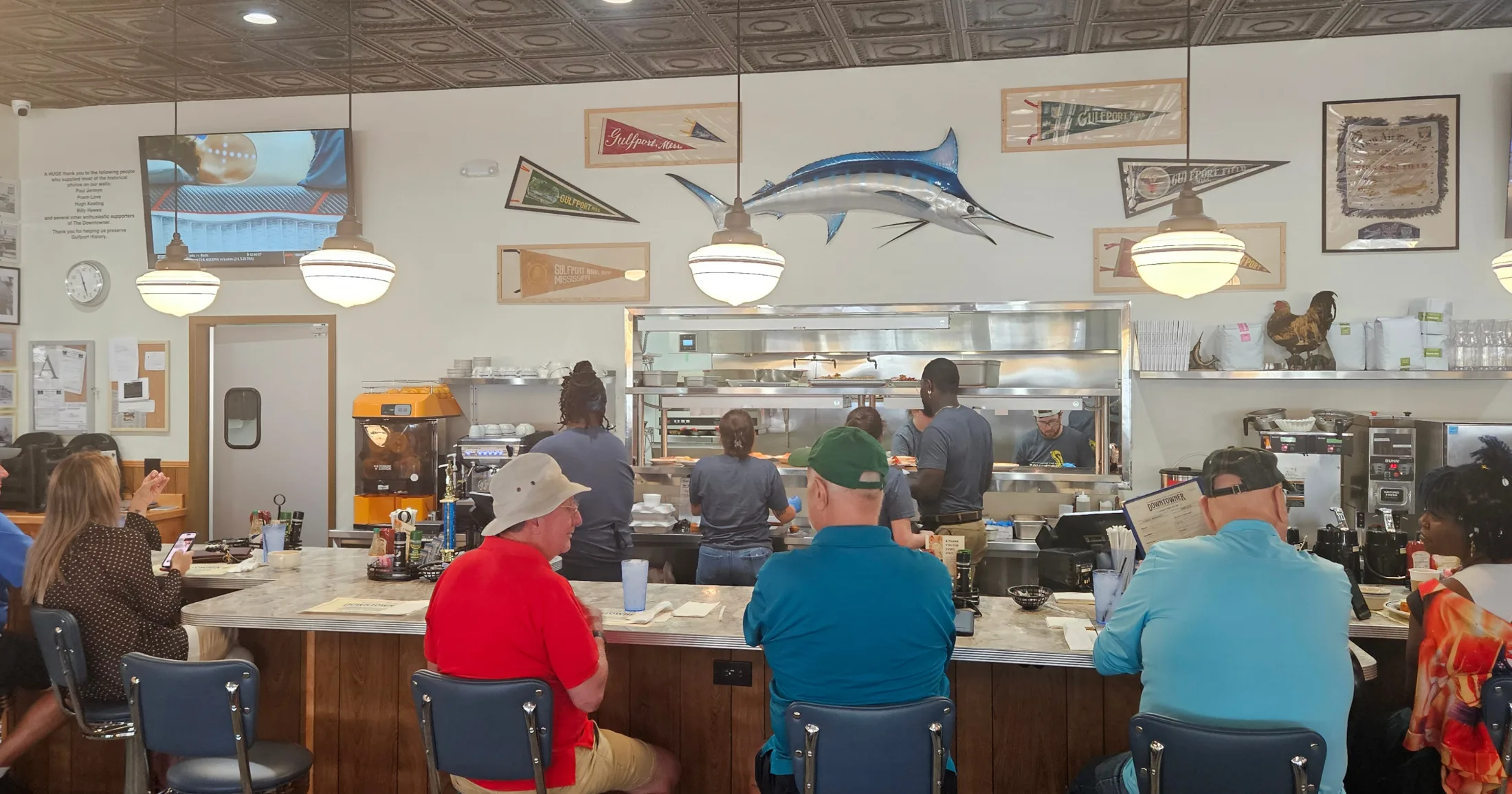 The Downtowner lunch counter with blue swivel stools, open kitchen, Gulfport pennants, and a mounted marlin above the pass