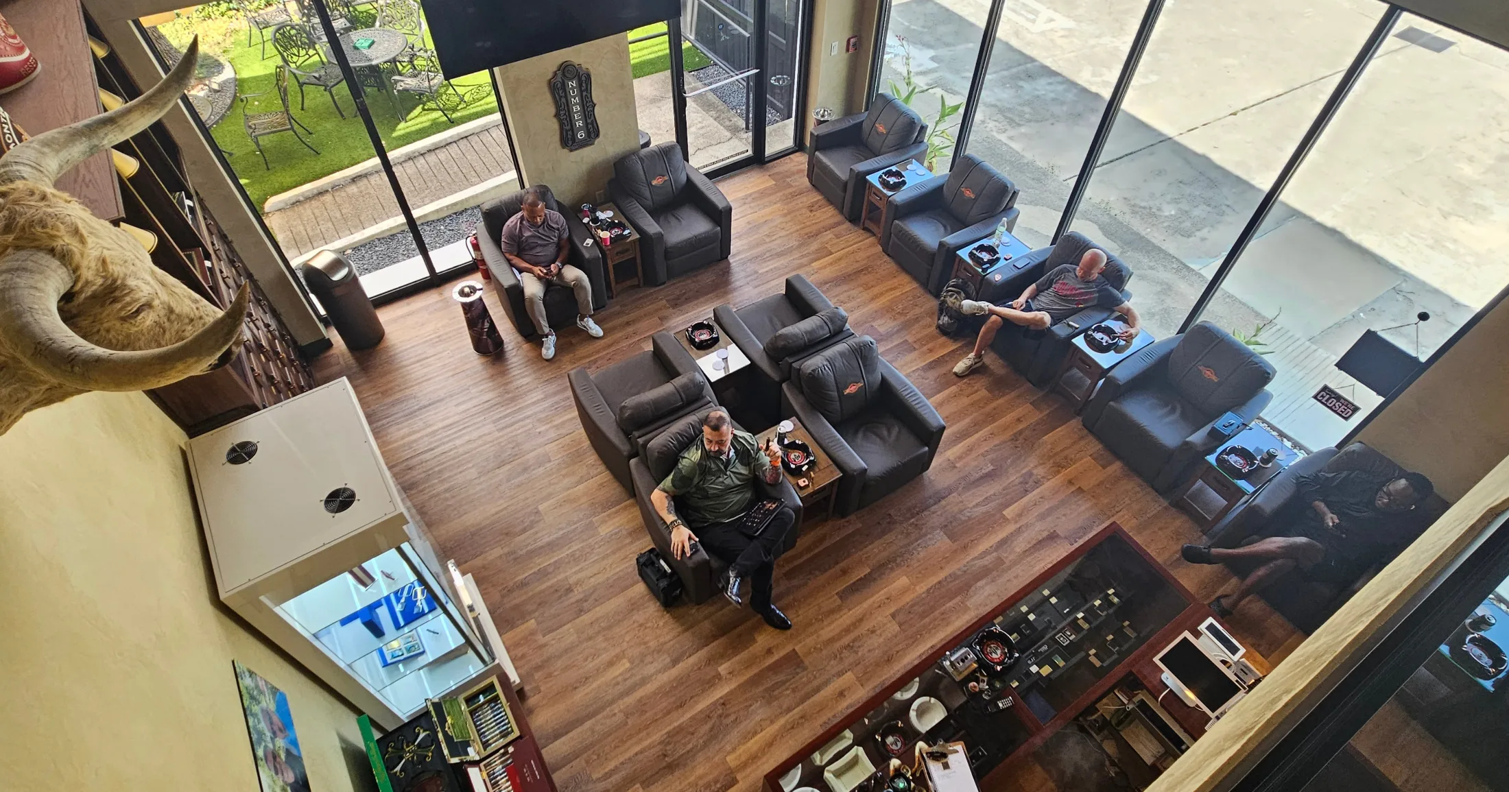 Aerial view of the main lounge floor looking down from the members-only upper level, outdoor garden visible through glass doors