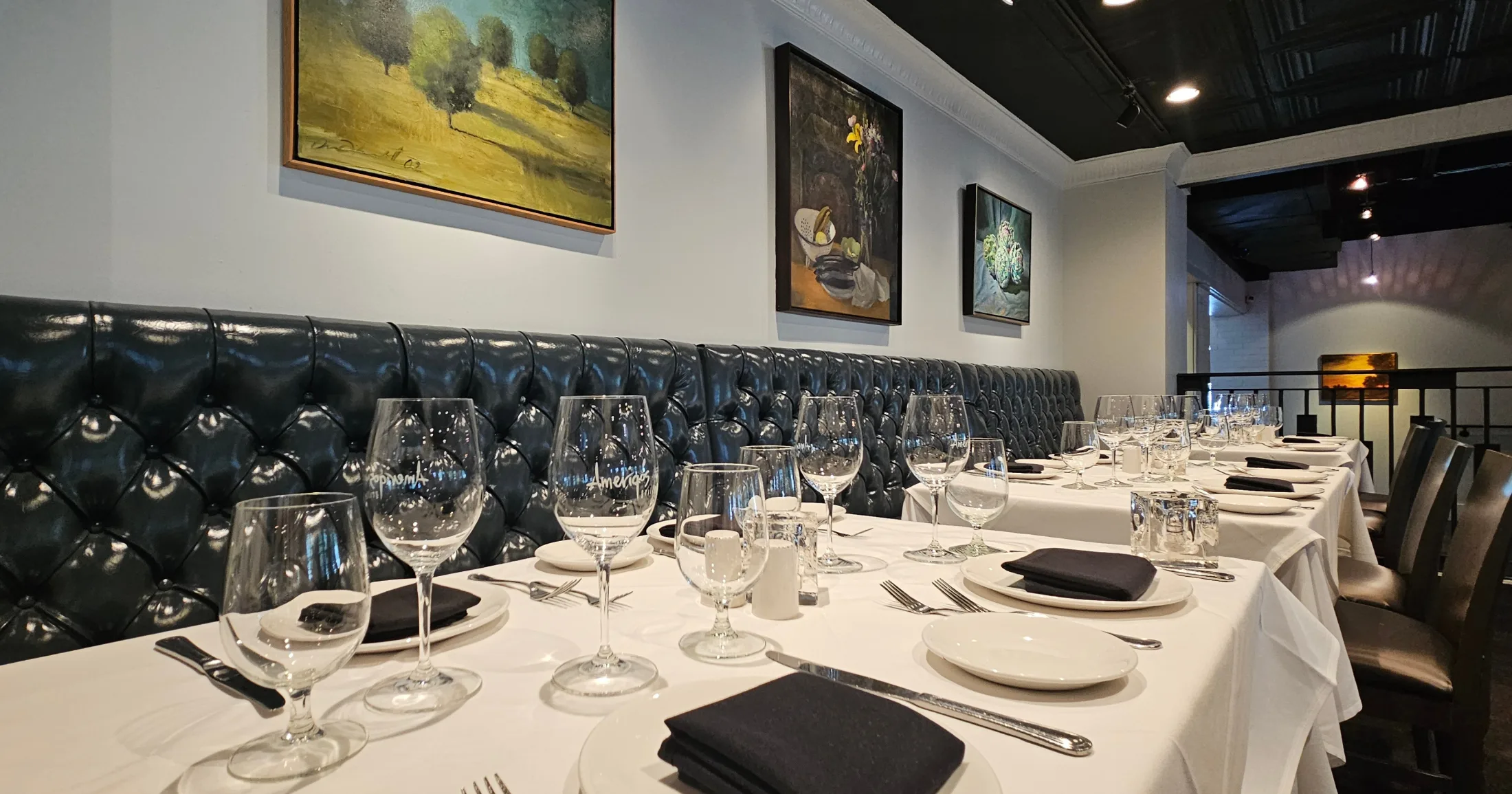 Tufted leather banquette and white-linen tables set with Amerigo's wine glasses in the dining room