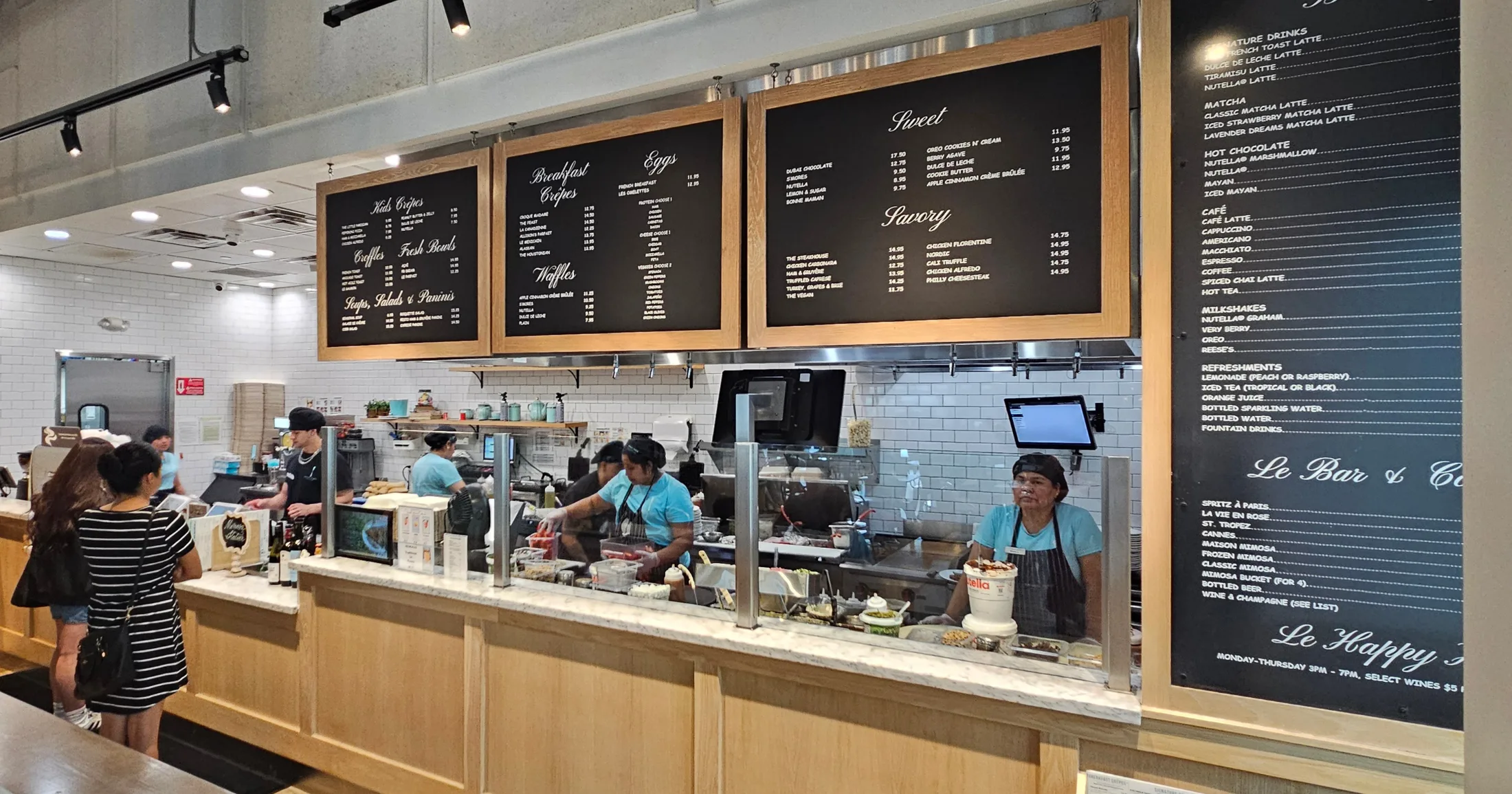 Sweet Paris interior counter with staff preparing crêpes behind glass, large menu boards above